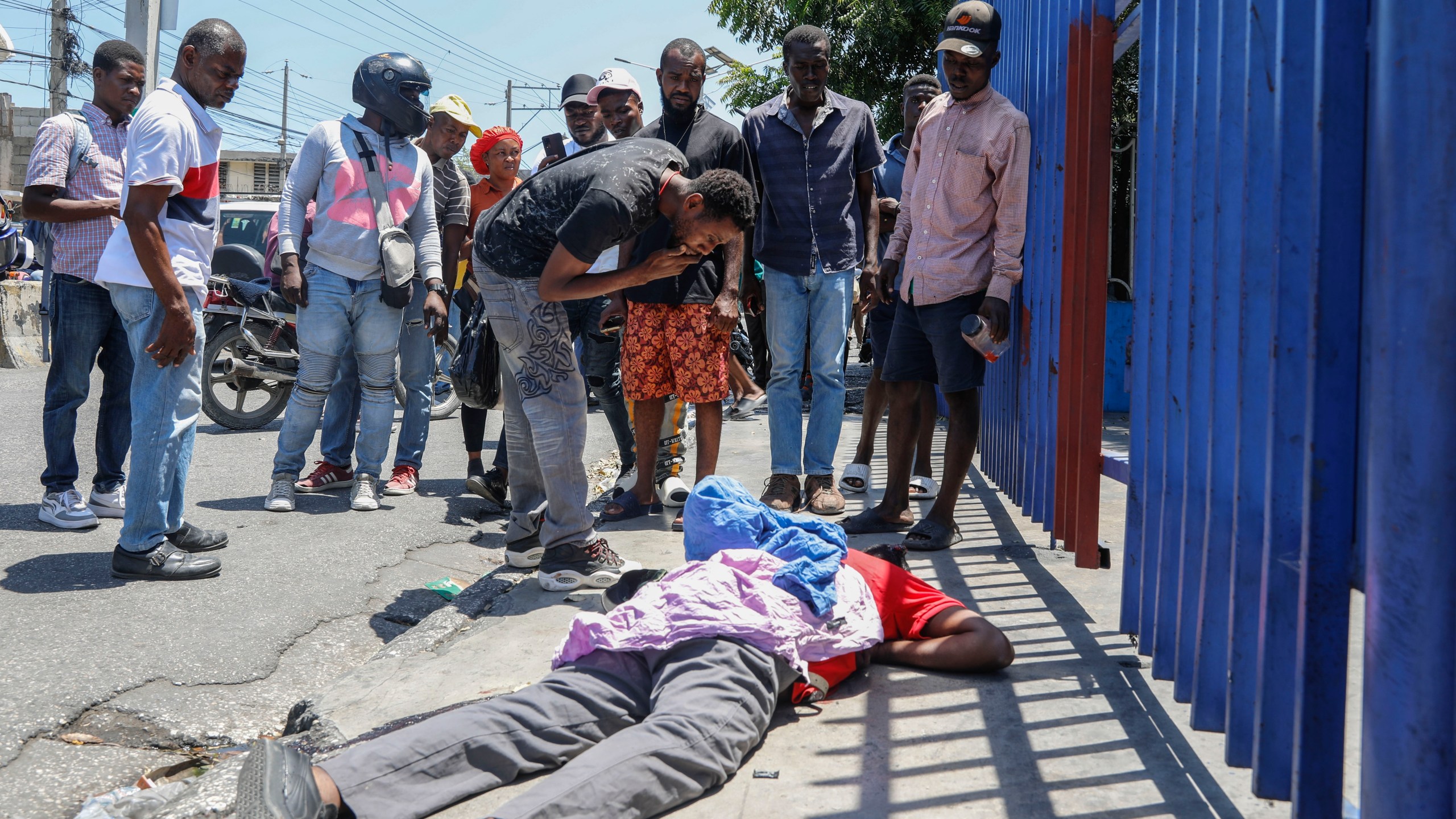People observe the body of a man lying on the street of the Delmas 30 neighborhood in Port-au-Prince, Haiti, Monday, April 1, 2024. Witnesses reported that he was struck by a stray bullet during a shootout between police and gangs. (AP Photo/Odelyn Joseph)