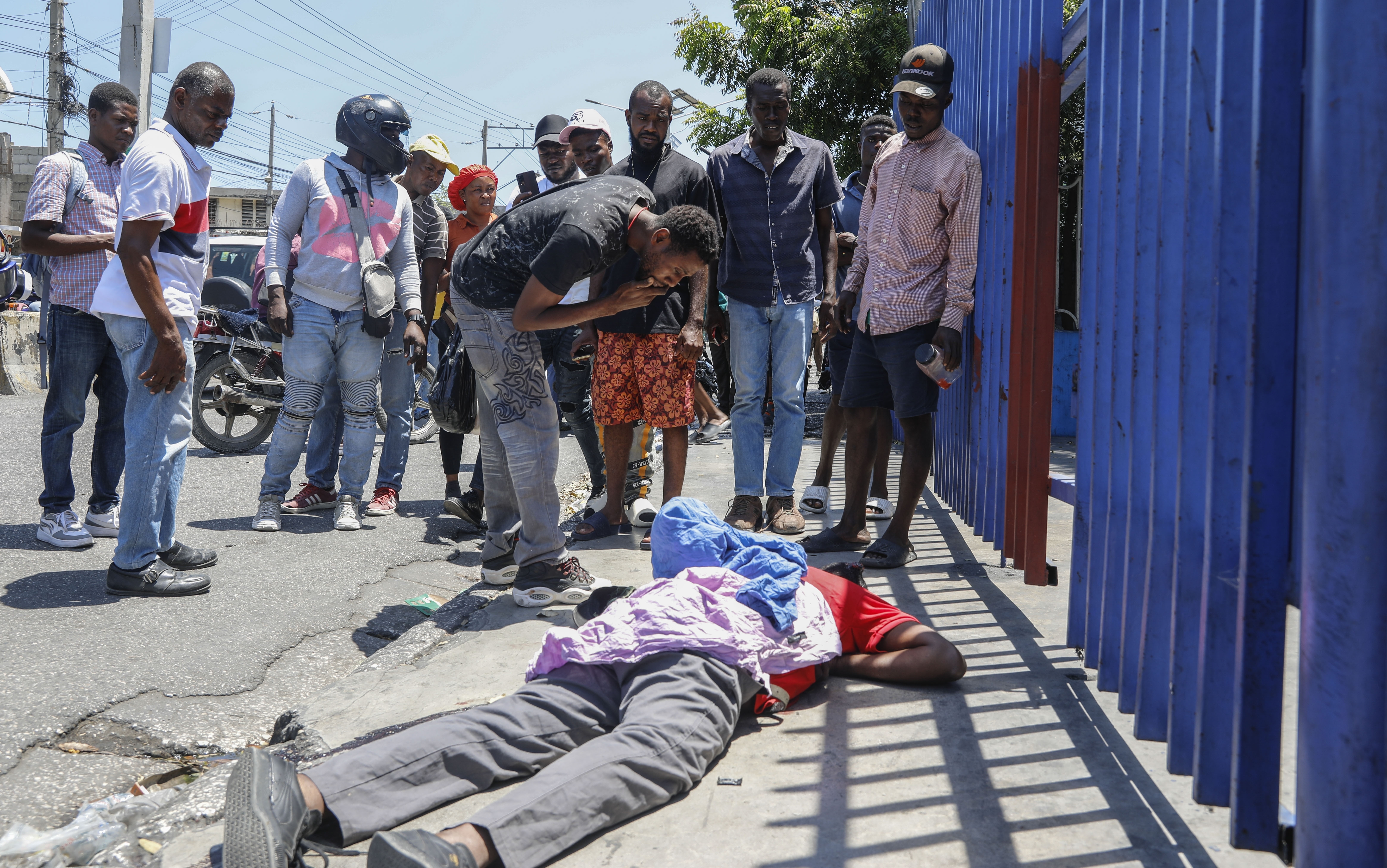 People observe the body of a man lying on the street of the Delmas 30 neighborhood in Port-au-Prince, Haiti, Monday, April 1, 2024. Witnesses reported that he was struck by a stray bullet during a shootout between police and gangs. (AP Photo/Odelyn Joseph)