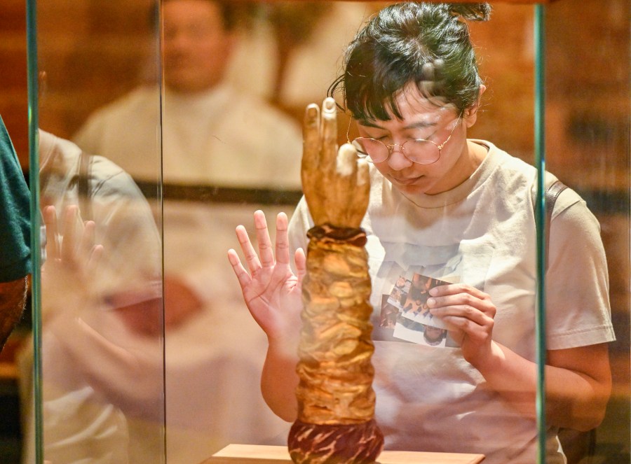 Melannie Rivamonte holds pictures of her family against the glass during a visit to the relic of St. Jude Thaddeus on display at Santiago de Compostela Catholic Church in Lake Forest, CA, on Monday, April 29, 2024.