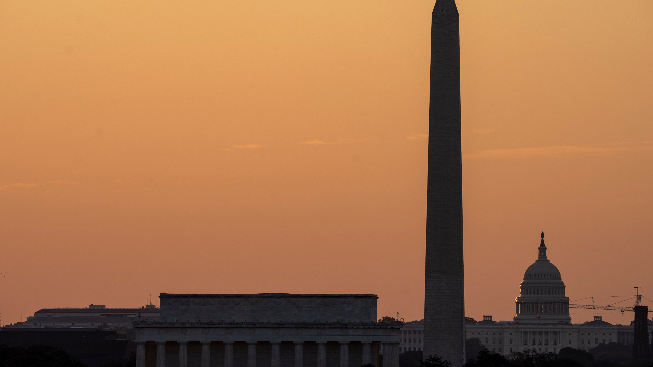 The sky glows orange as the sun rises near the U.S. Capitol, Washington Monument and Lincoln Memorial in Washington, Friday, June 21, 2024, as seen from Arlington, Va. The National Weather Service said scorching temperatures will linger across the Ohio Valley and Mid-Atlantic region. (AP Photo/Alex Brandon)