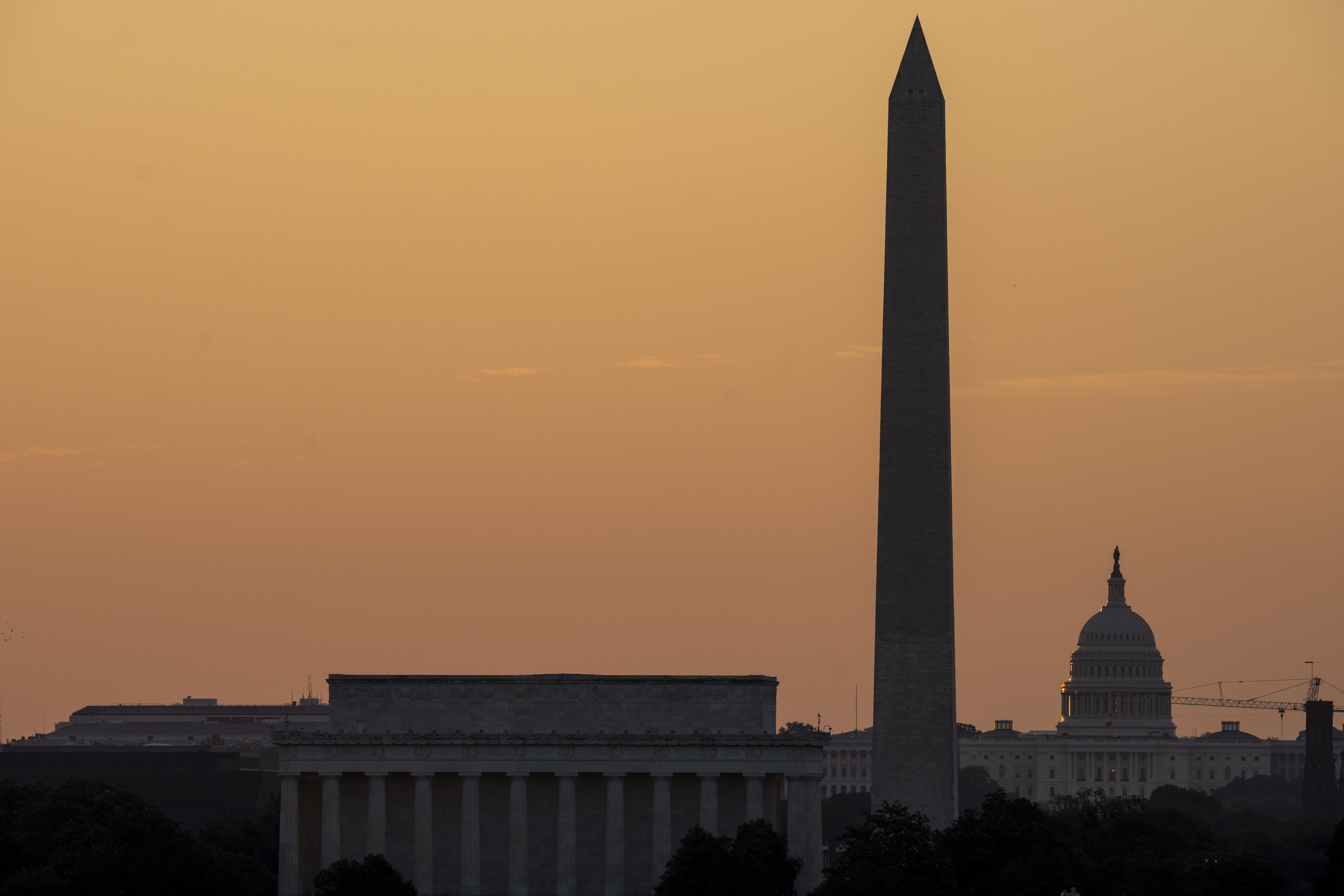The sky glows orange as the sun rises near the U.S. Capitol, Washington Monument and Lincoln Memorial in Washington, Friday, June 21, 2024, as seen from Arlington, Va. The National Weather Service said scorching temperatures will linger across the Ohio Valley and Mid-Atlantic region. (AP Photo/Alex Brandon)