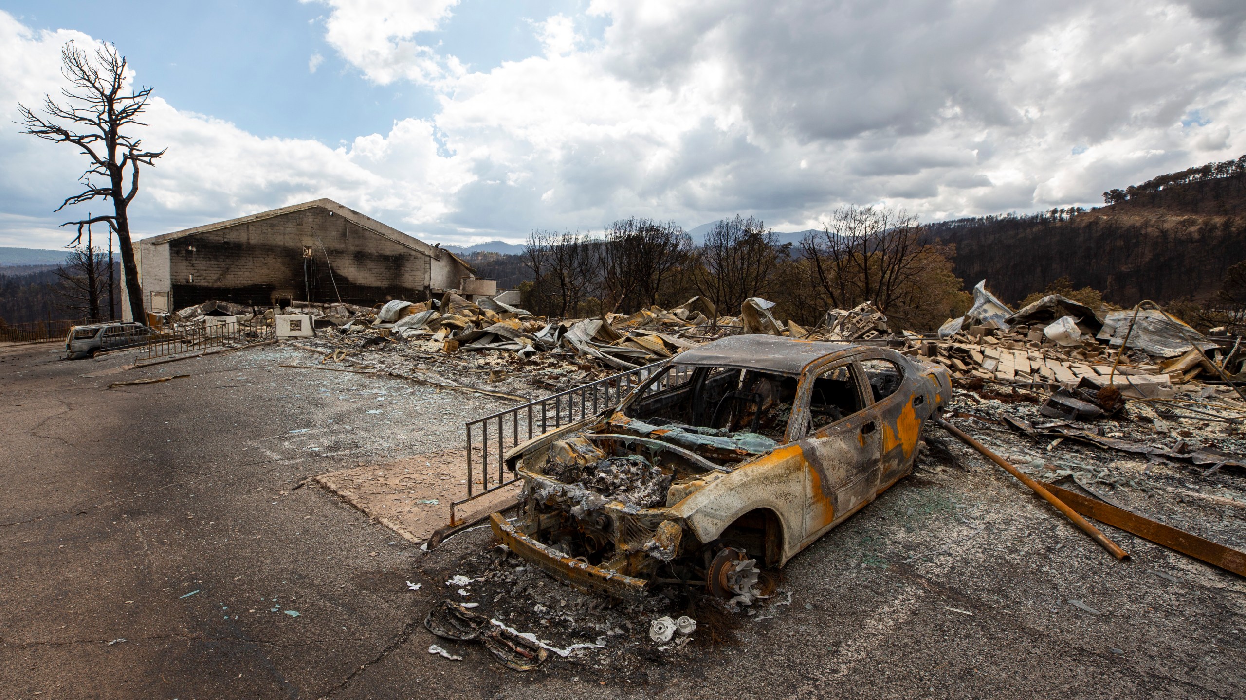 A charred car and the remains of the Swiss Chalet Hotel are pictured after being destroyed by the South Fork Fire in the mountain village of Ruidoso, N.M., Saturday, June 22, 2024. (AP Photo/Andres Leighton)