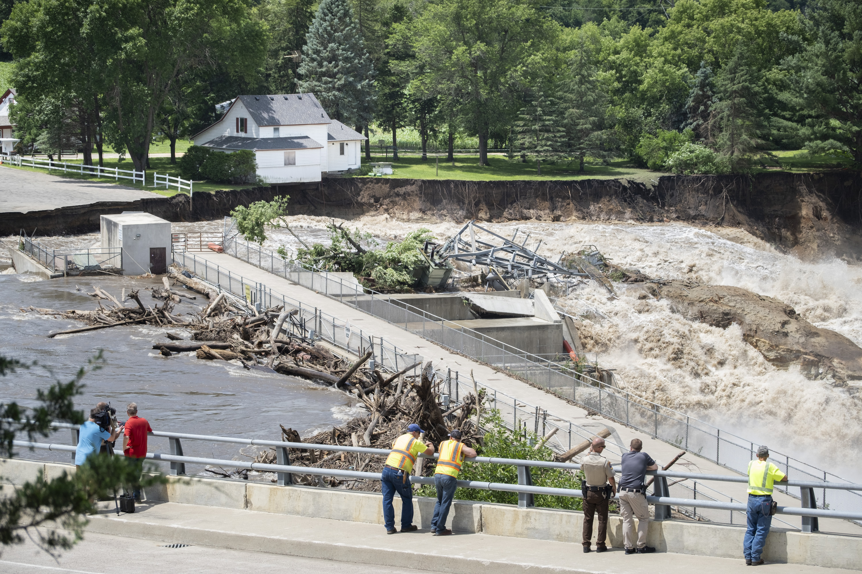 Onlookers take in the catastrophic damage to the Rapidan Dam site in Rapidan, Minn., Monday, June 24, 2024. Debris blocked the dam forcing the heavily backed up waters of the Blue Earth River to reroute along the bank nearest the Dam Store. (Casey Ek/The Free Press via AP)