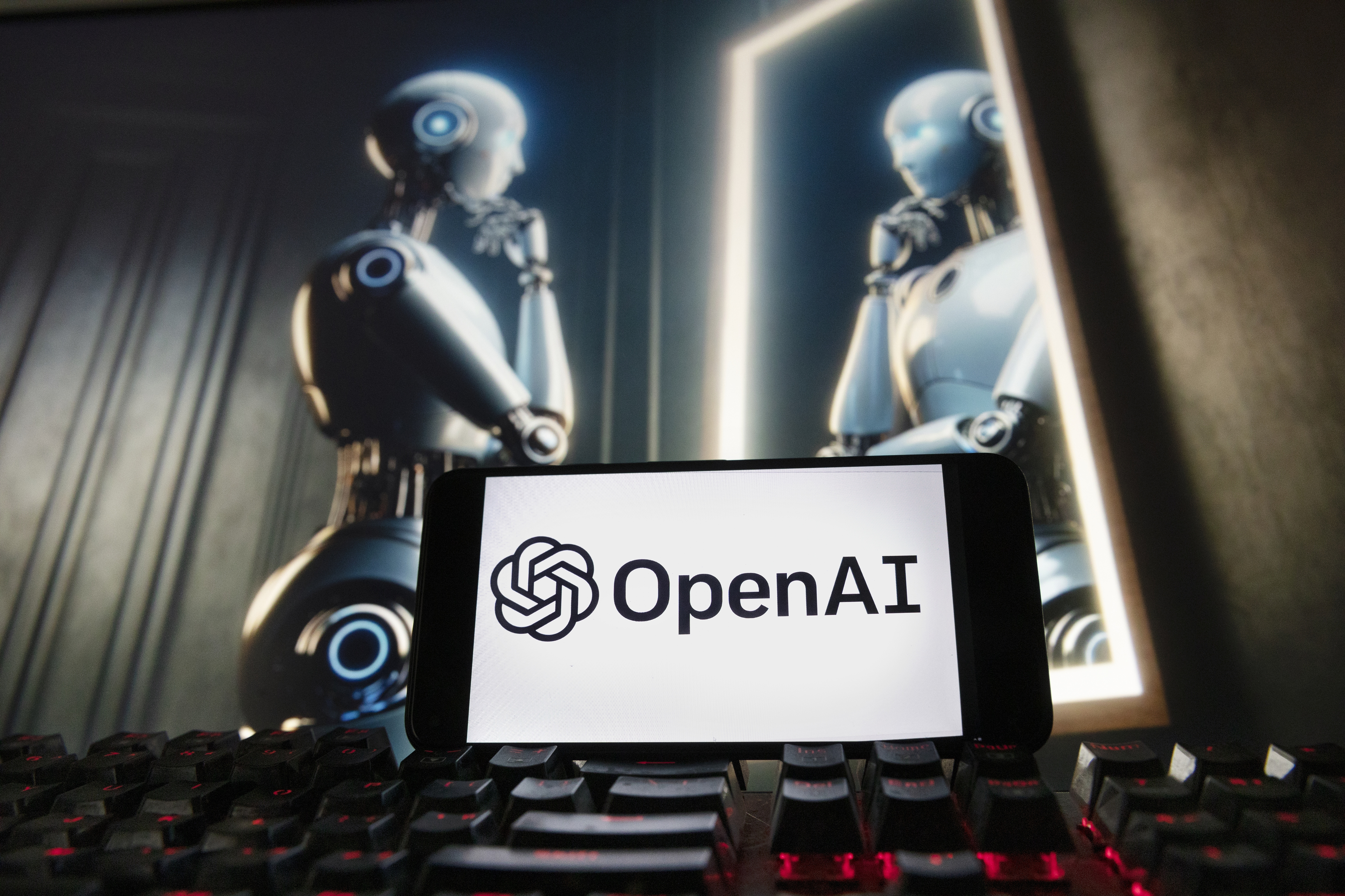 FILE- The OpenAI logo is displayed on a cell phone with an image on a computer monitor generated by ChatGPT's Dall-E text-to-image model, Dec. 8, 2023, in Boston. The European Union is escalating its scrutiny of the artificial intelligence industry, including taking a fresh look into Microsoft’s multibillion-dollar partnership with OpenAI. The bloc started reviewing the multibillion-dollar deal last year to see whether it broke EU merger rules but dropped it after concluding Microsoft hadn’t gained control of OpenAI. (AP Photo/Michael Dwyer, File)