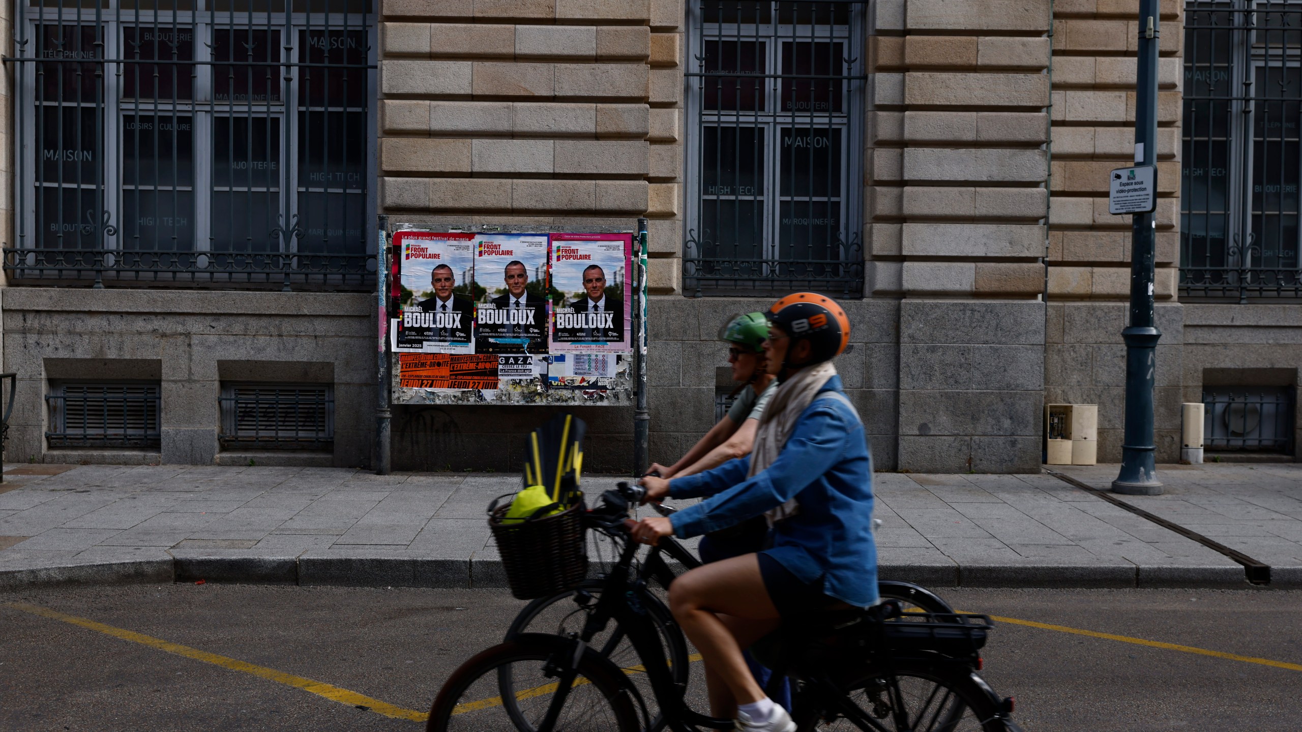 Two people ride a bicycle in front of an electoral panel in Rennes, western France, Sunday June 30, 2024.France is holding the first round of an early parliamentary election on Sunday that could bring the country's first far-right government since Nazi occupation during World War II.The second round is on July 7, and the outcome of the vote remains highly uncertain. (AP Photo/Jeremias Gonzalez)
