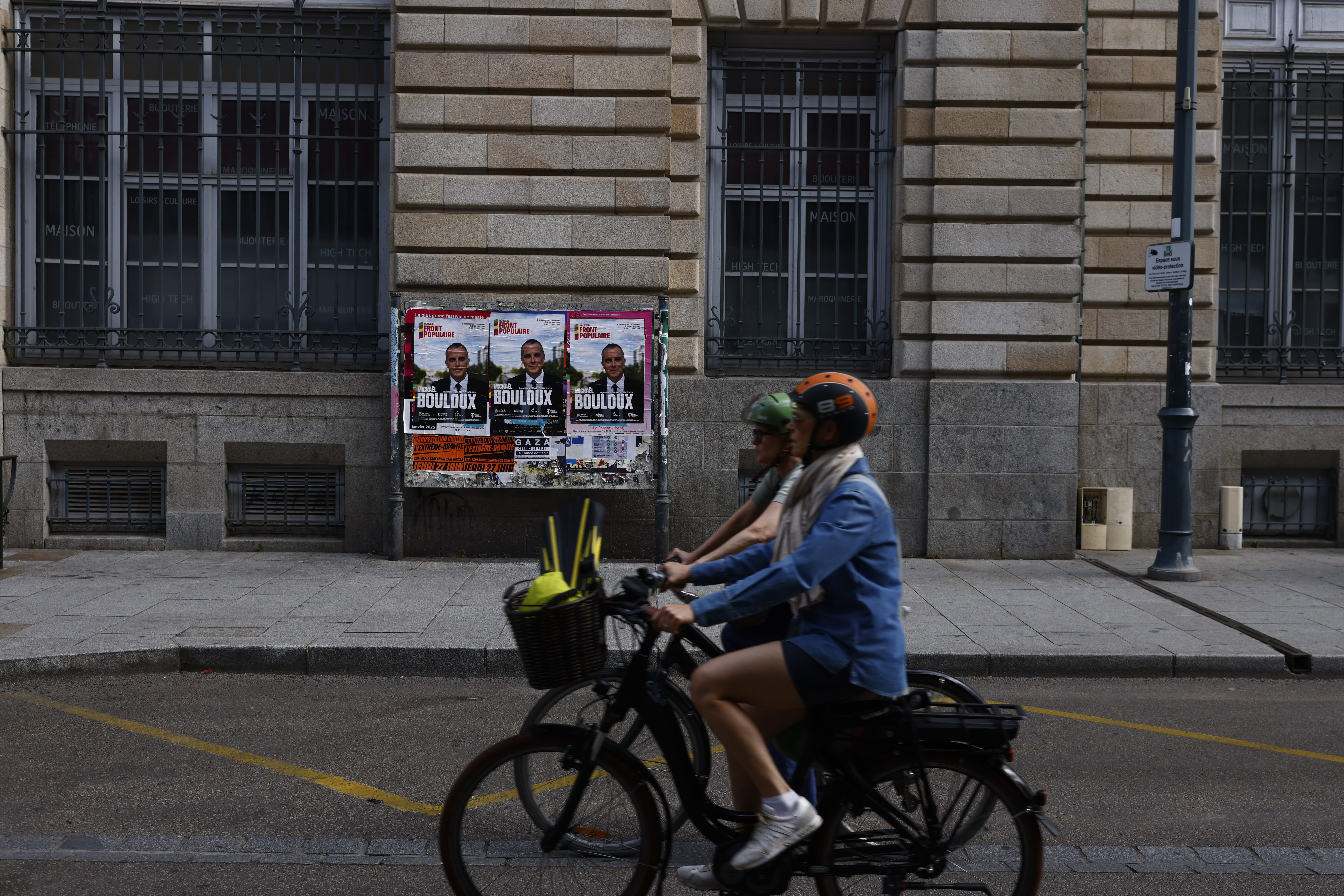 Two people ride a bicycle in front of an electoral panel in Rennes, western France, Sunday June 30, 2024.France is holding the first round of an early parliamentary election on Sunday that could bring the country's first far-right government since Nazi occupation during World War II.The second round is on July 7, and the outcome of the vote remains highly uncertain. (AP Photo/Jeremias Gonzalez)
