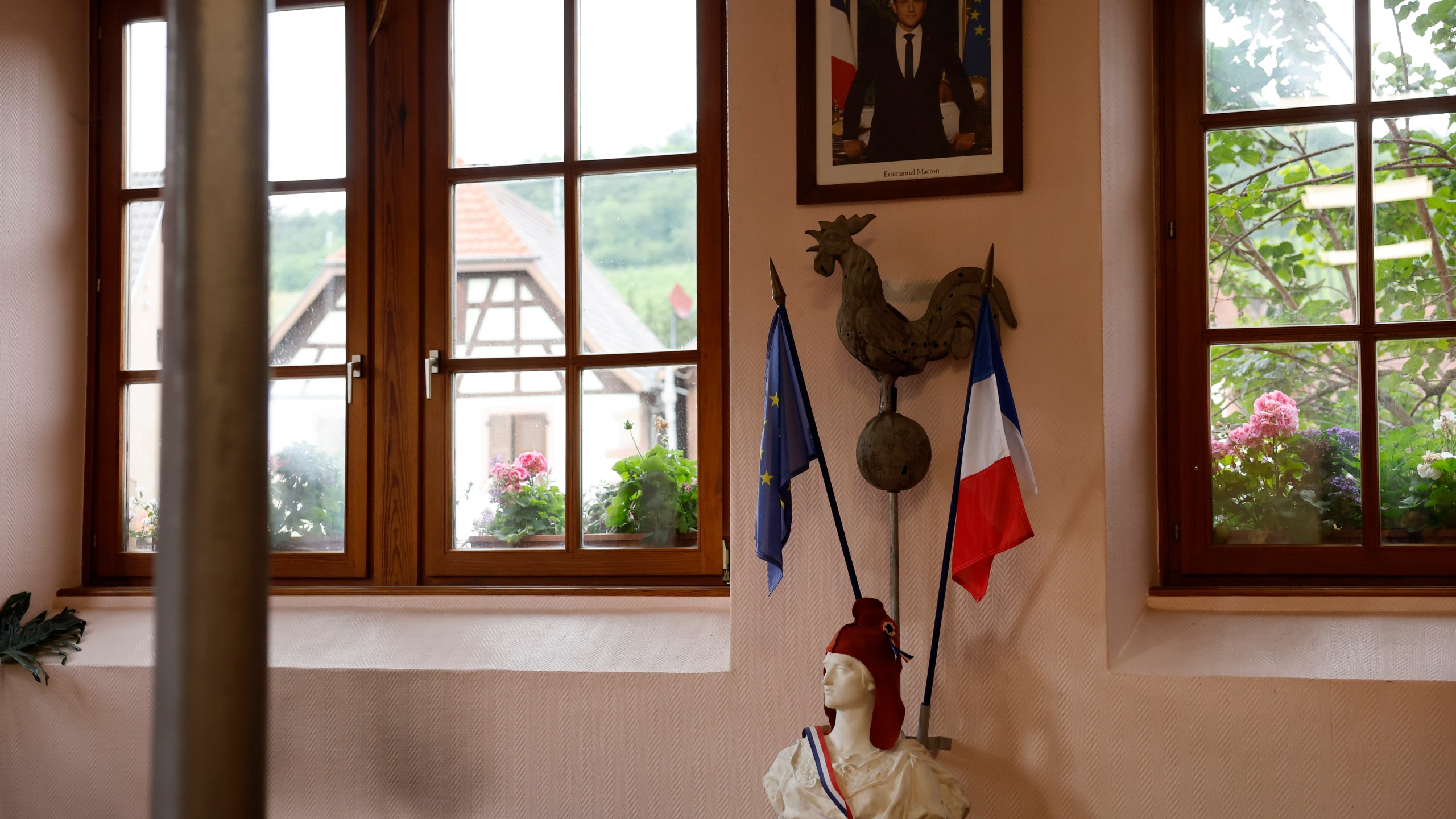 A portrait of French President Emmanuel Macron hangs above a statue of Marianne and a rooster, symbols of the French Republic and France, in a voting station in Soultz-Les-Bains, eastern France, Sunday, June 30, 2024. France is holding the first round of an early parliamentary election on Sunday that could bring the country's first far-right government since Nazi occupation during World War II. The second round is on July 7, and the outcome of the vote remains highly uncertain. (AP Photo/Jean-Francois Badias)