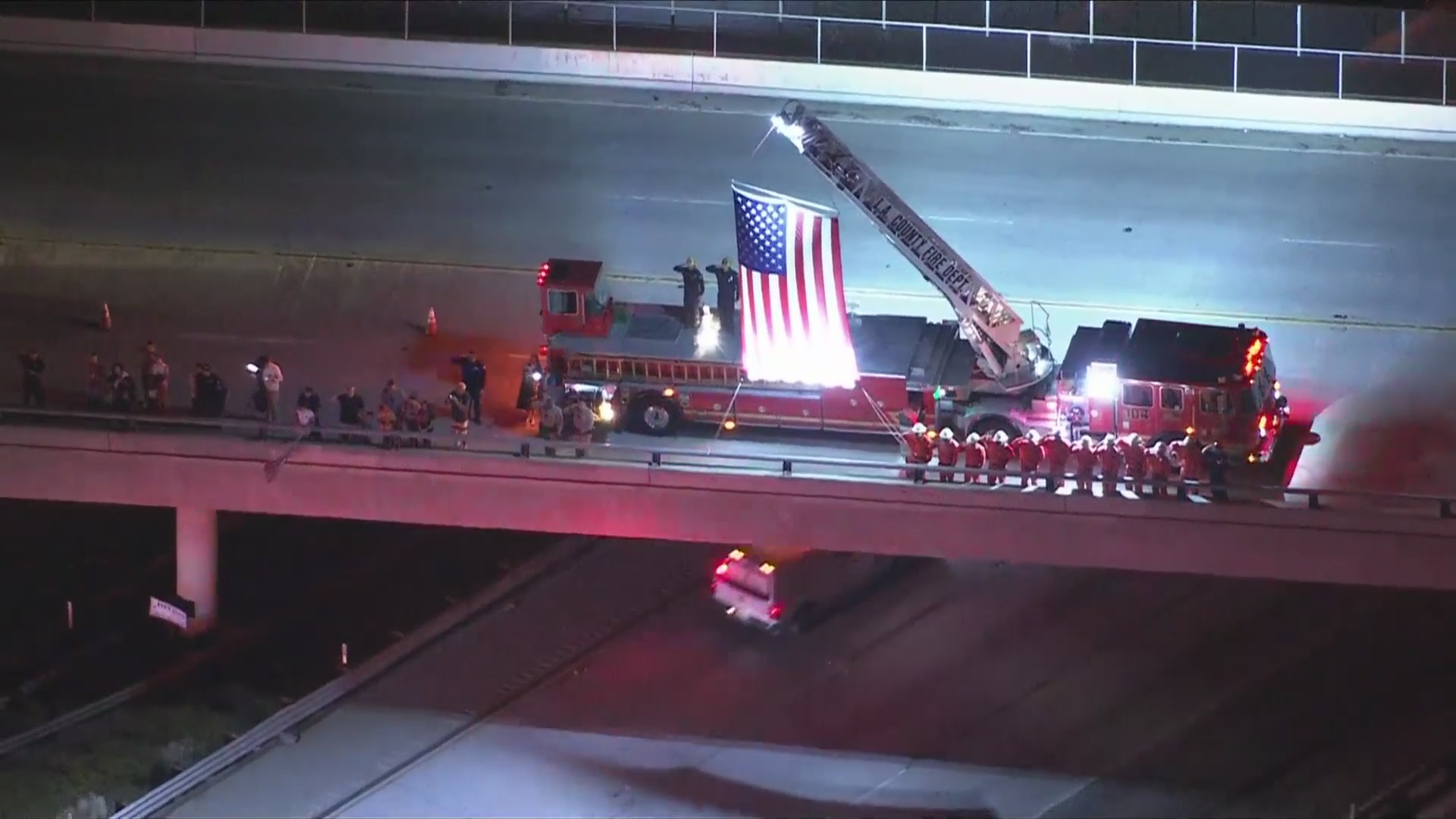 Firefighters lifting an American flag and saluting Andrew Pontious as a procession passes by on June 14, 2024. (KTLA)