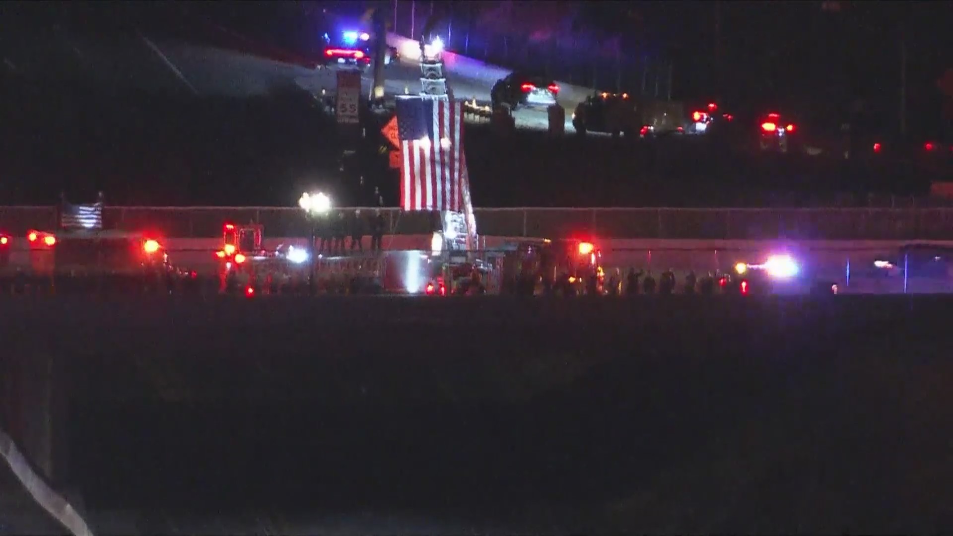 More firefighters lifting an American flag and saluting Andrew Pontious on a freeway overpass as a procession passes by underneath them on June 14, 2024. (KTLA)