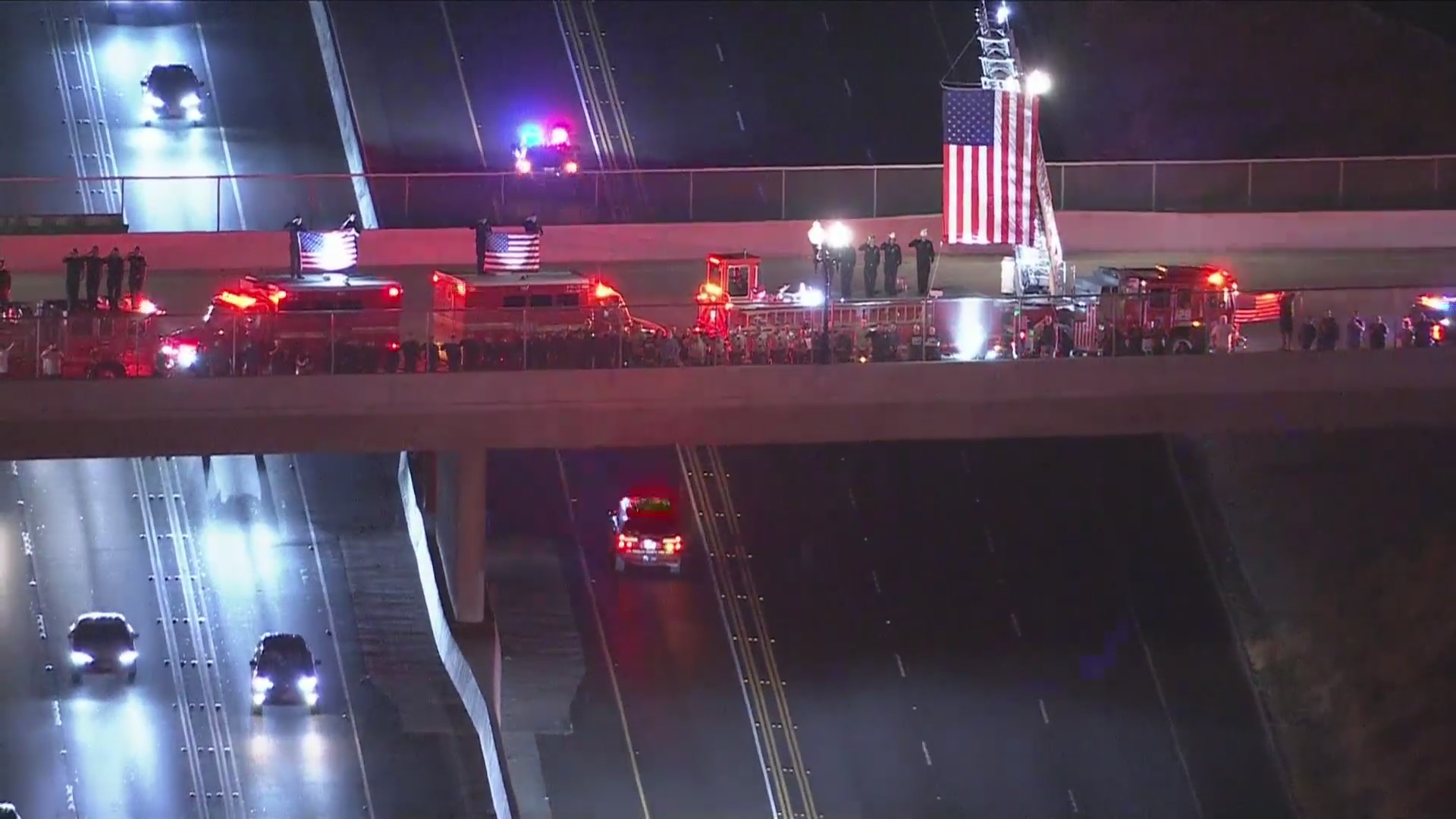 More firefighters lifting an American flag and saluting Andrew Pontious on a freeway overpass as a procession passes by underneath them on June 14, 2024. (KTLA)