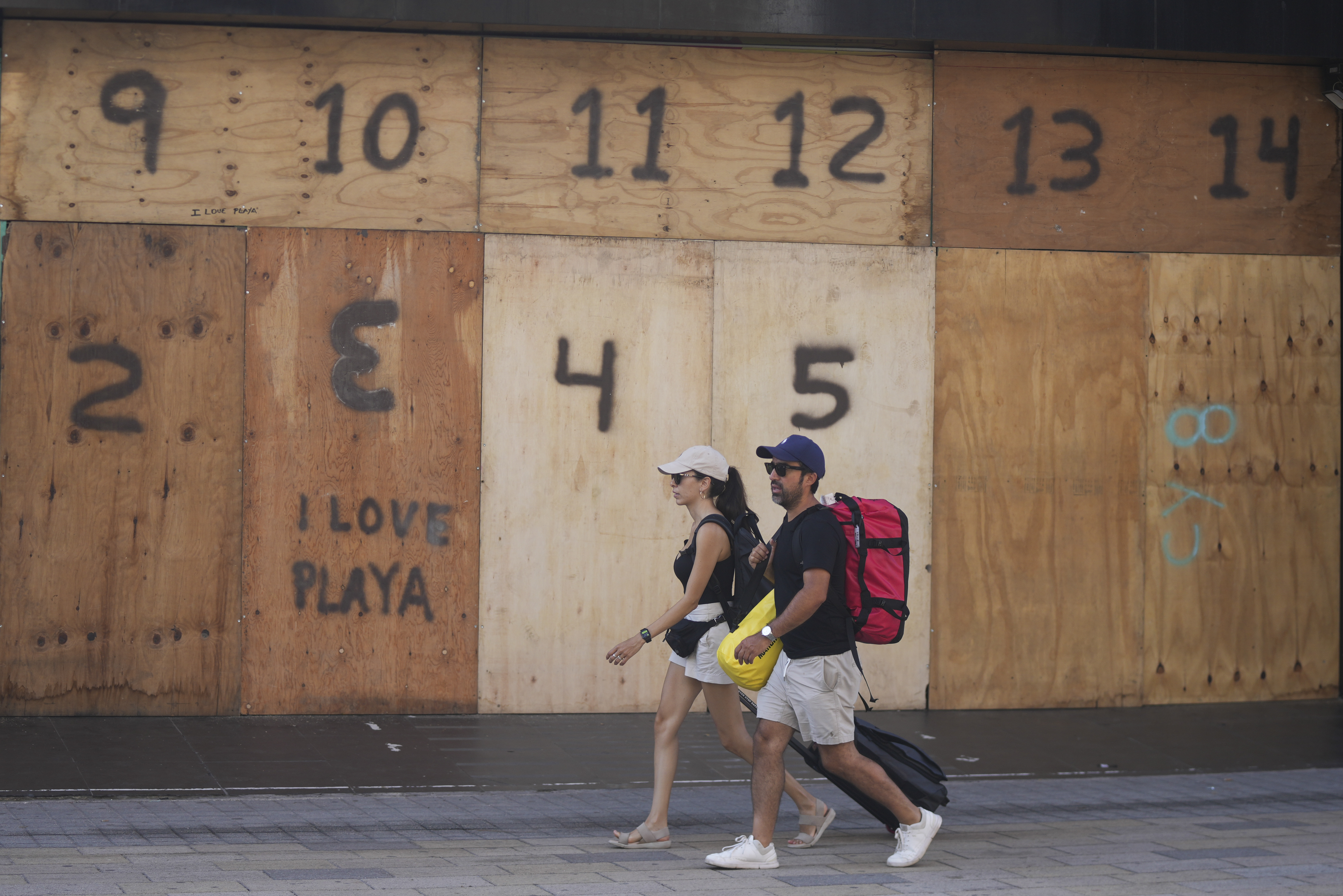 People walk past a souvenir shop's storefront boarded up preparation for the arrival of Hurricane Beryl, in Playa del Carmen, Mexico, Thursday, July 4, 2024. (AP Photo/Fernando Llano)