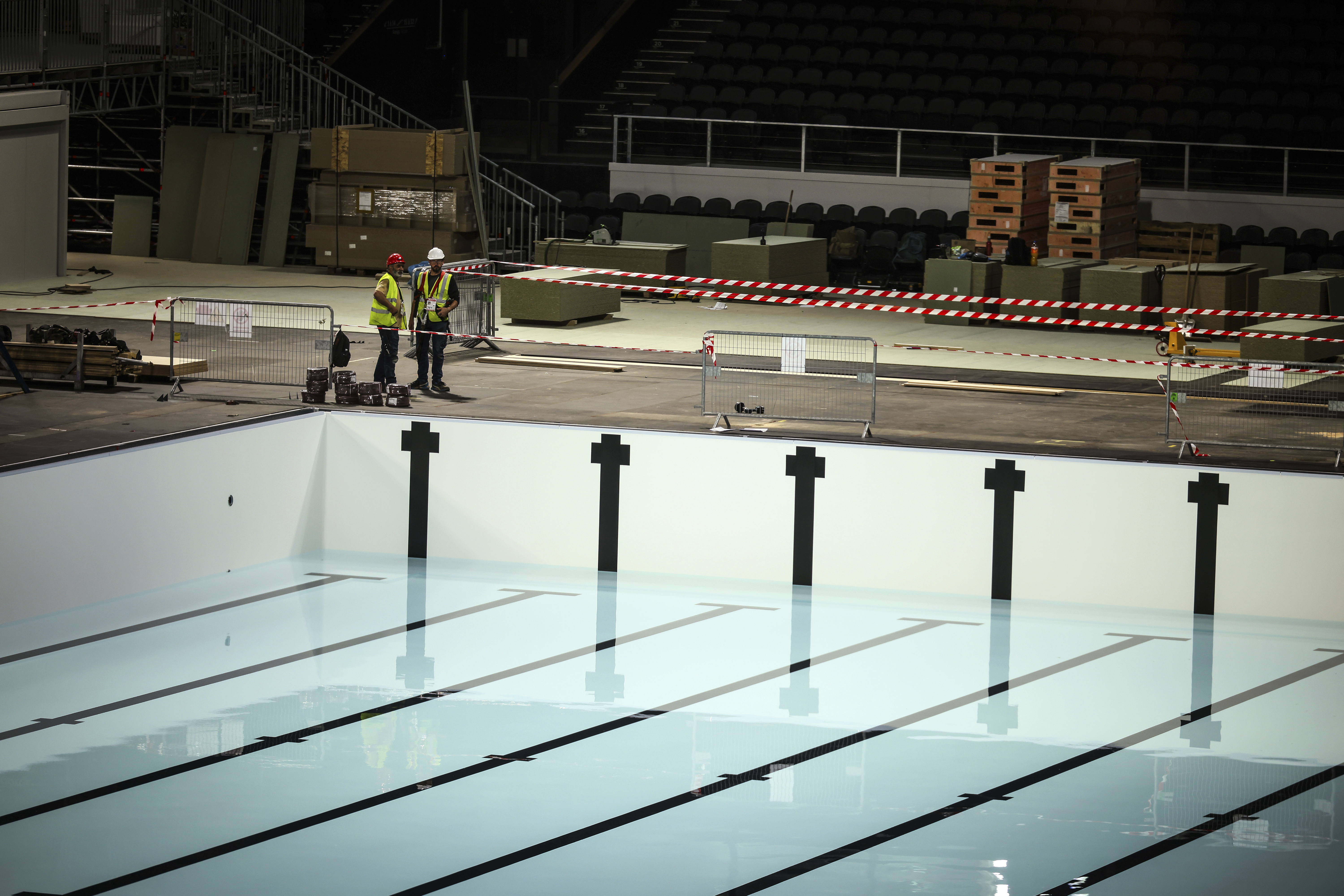 Workers stand by the olympic swimming pool, Wednesday, June 12, 2024 at the Paris La Defense Arena, in Nanterre, outside Paris. The Paris La Defense Arena will host the swimming and some water polo events during the Paris 2024 Olympic Games. (AP Photo/Thomas Padilla)