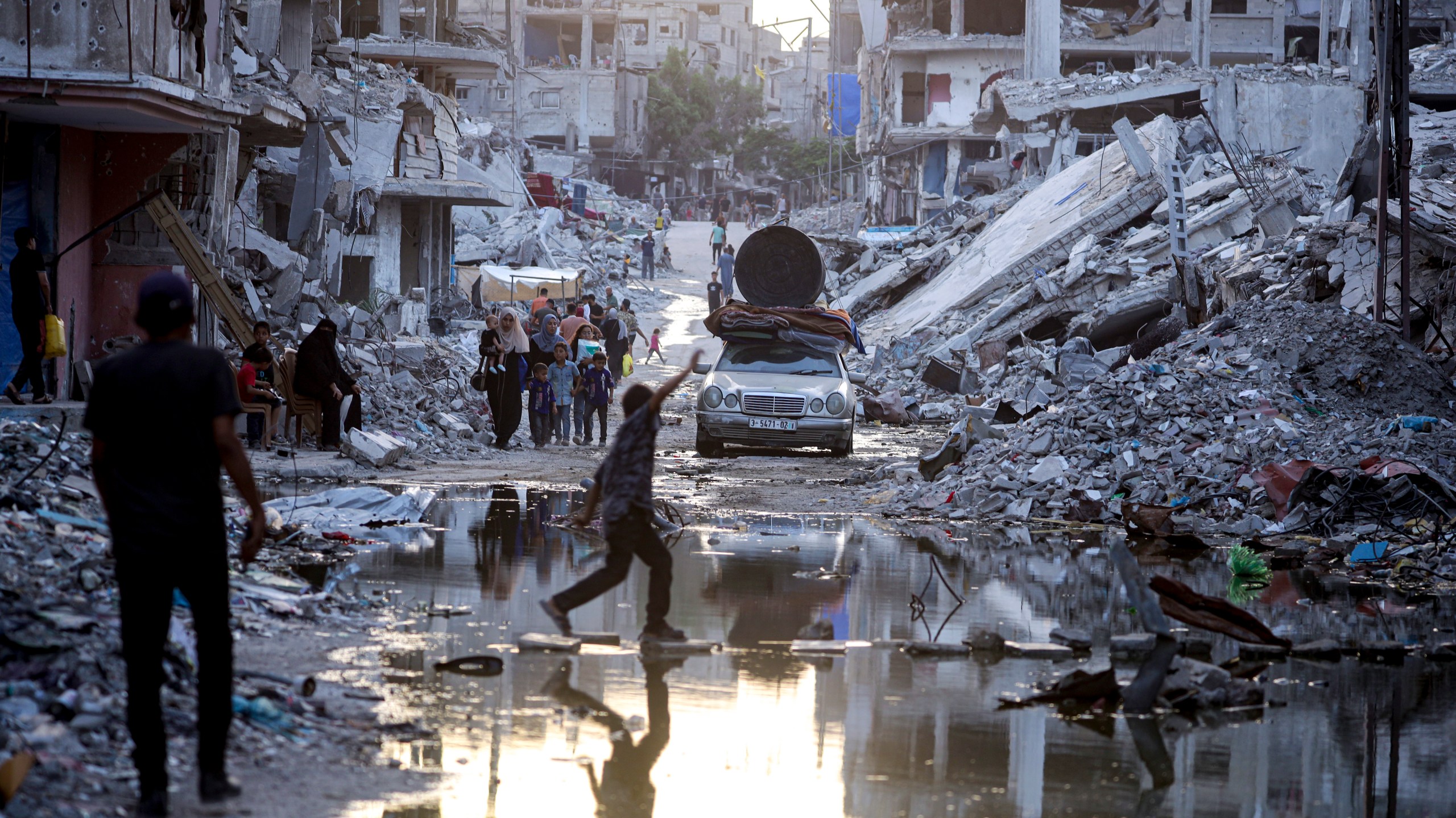 Palestinians displaced by the Israeli air and ground offensive on the Gaza Strip, walk past sewage flowing into the streets of the southern town of Khan Younis, Gaza Strip, Thursday, July 4, 2024. (AP Photo/Jehad Alshrafi)