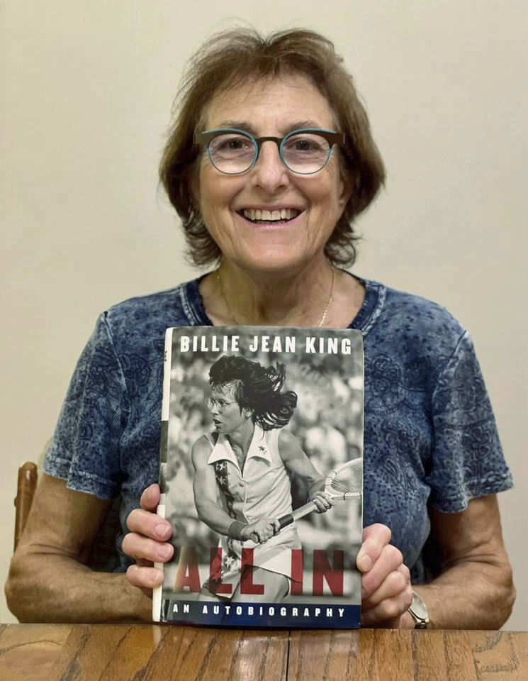 In this 2021 photo provided by the Willens family, Kathy Willens poses for a photo with a copy of Billie Jean King's autobiography "All In" with an image Willens took of King in 1977 on the cover. (Willens family via AP)