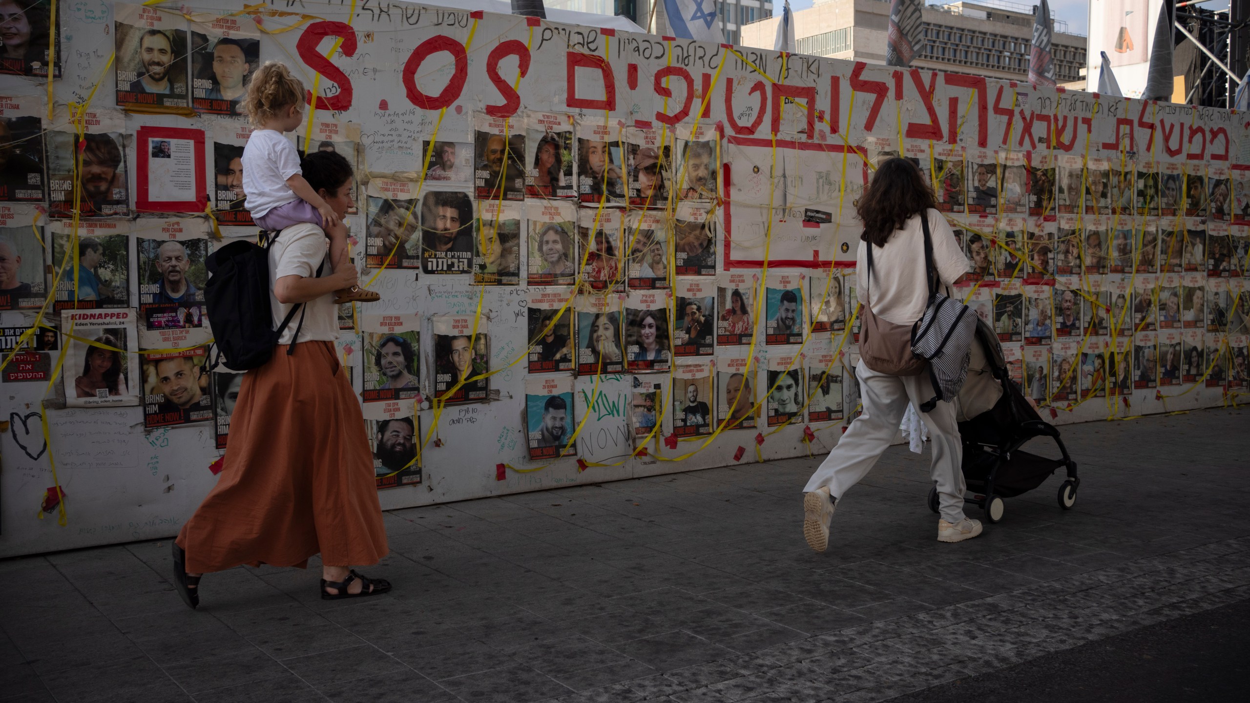 People walk past a wall with photos of hostages held in the Gaza Strip at a plaza known as Hostages Square in Tel Aviv, Israel Tuesday, July 16, 2024. (AP Photo/Leo Correa)