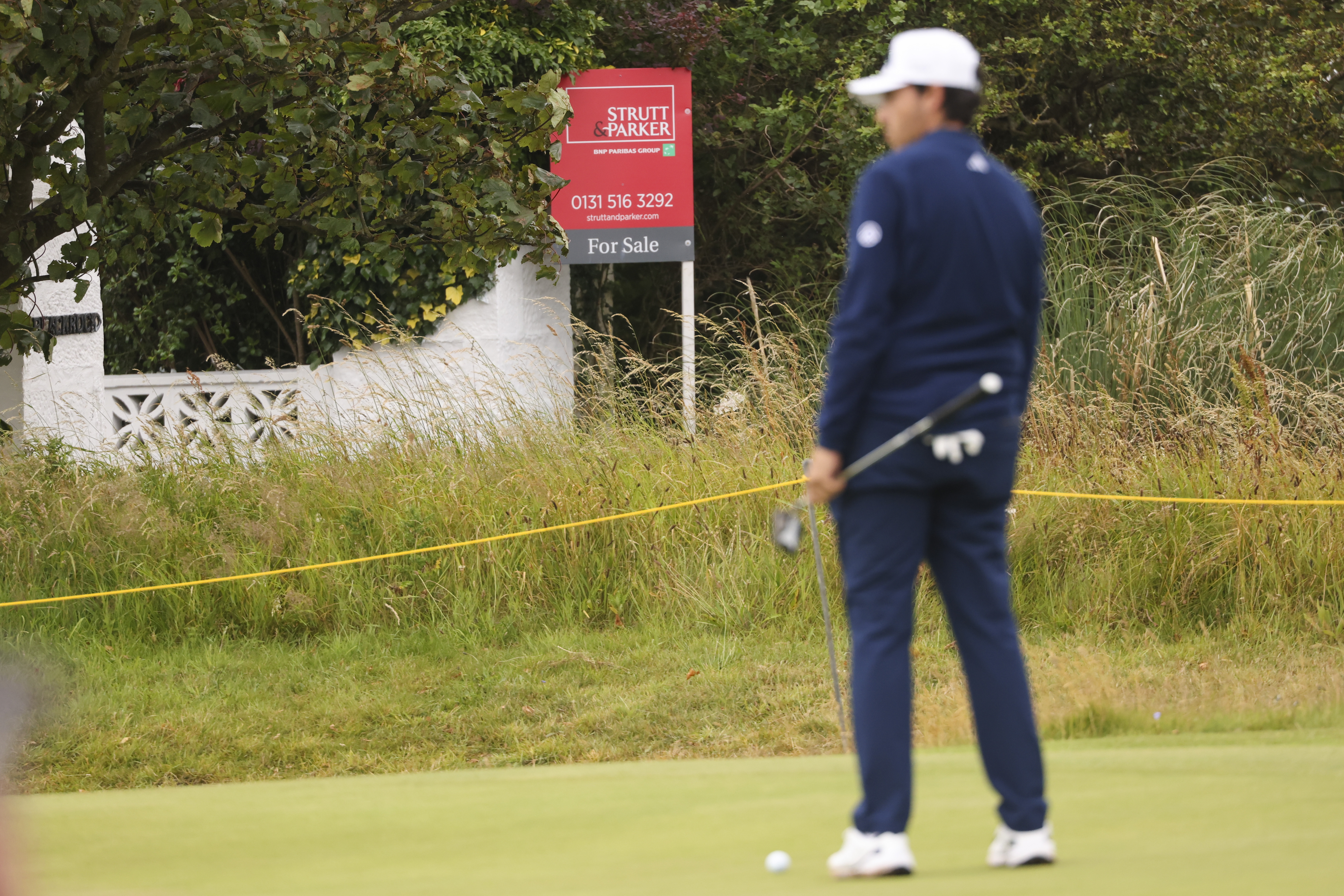 A golfer waits to putt on the 17th green, near "Blackrock house" that is listed for sale near the second and 16th holes at Royal Troon golf club, venue for the British Open Golf Championships, in Troon, Scotland, Tuesday, July 16, 2024. Royal Troon has some unique aspects but maybe most curious is the private house that sits in the middle of the championship course and has views of five holes. (AP Photo/Peter Morrison)