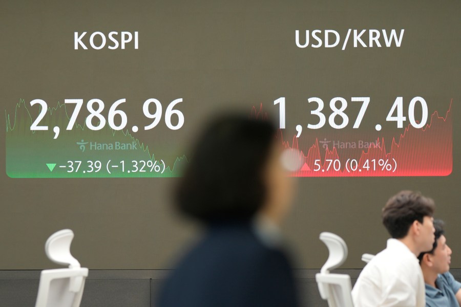 A currency trader walks by the screens showing the Korea Composite Stock Price Index (KOSPI), left, and the foreign exchange rate between U.S. dollar and South Korean won at a foreign exchange dealing room in Seoul, South Korea, Friday, July 19, 2024. (AP Photo/Lee Jin-man)