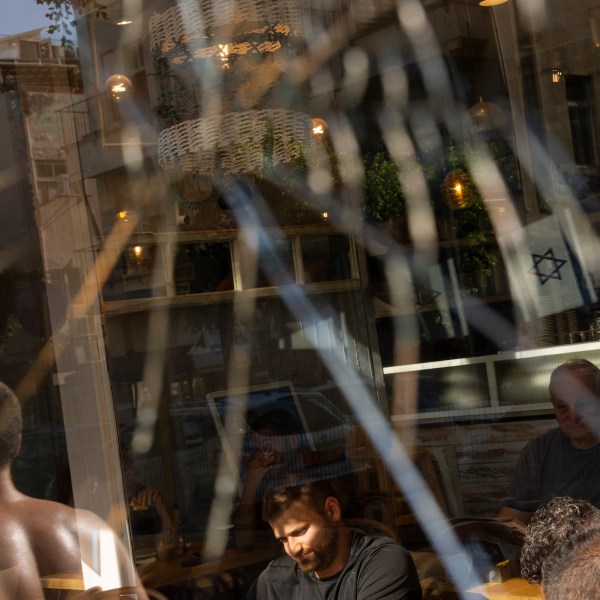 People are seen through a broken coffee shop window next to the scene of an explosive drone attack in Tel Aviv, Israel, Friday, July 19, 2024. Yemen's Houthi rebels claimed responsibility for a drone believed to have exploded above Tel Aviv early Friday morning. (AP Photo/Oded Balilty)