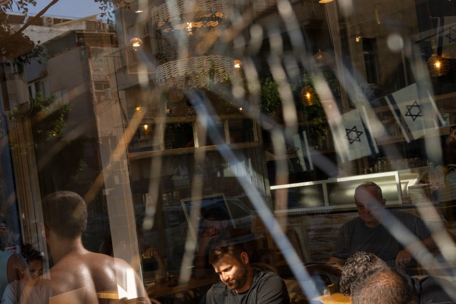 People are seen through a broken coffee shop window next to the scene of an explosive drone attack in Tel Aviv, Israel, Friday, July 19, 2024. Yemen's Houthi rebels claimed responsibility for a drone believed to have exploded above Tel Aviv early Friday morning. (AP Photo/Oded Balilty)