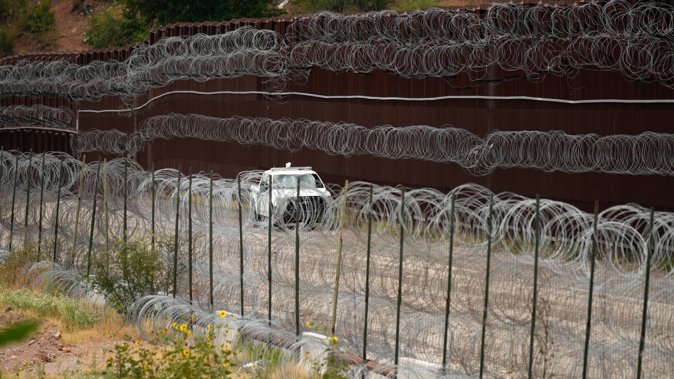 FILE - A vehicle drives along the U.S. side of the US-Mexico border wall in Nogales, Ariz. on Tuesday, June 25, 2024. Immigrant advocacy groups this week appealed a judge's ruling to allow the proposal to allow local law enforcement to arrest migrants who cross illegally from Mexico into Arizona between ports of entry to stay on the state's Nov. 5 ballot. (AP Photo/Jae C. Hong, Pool, File)