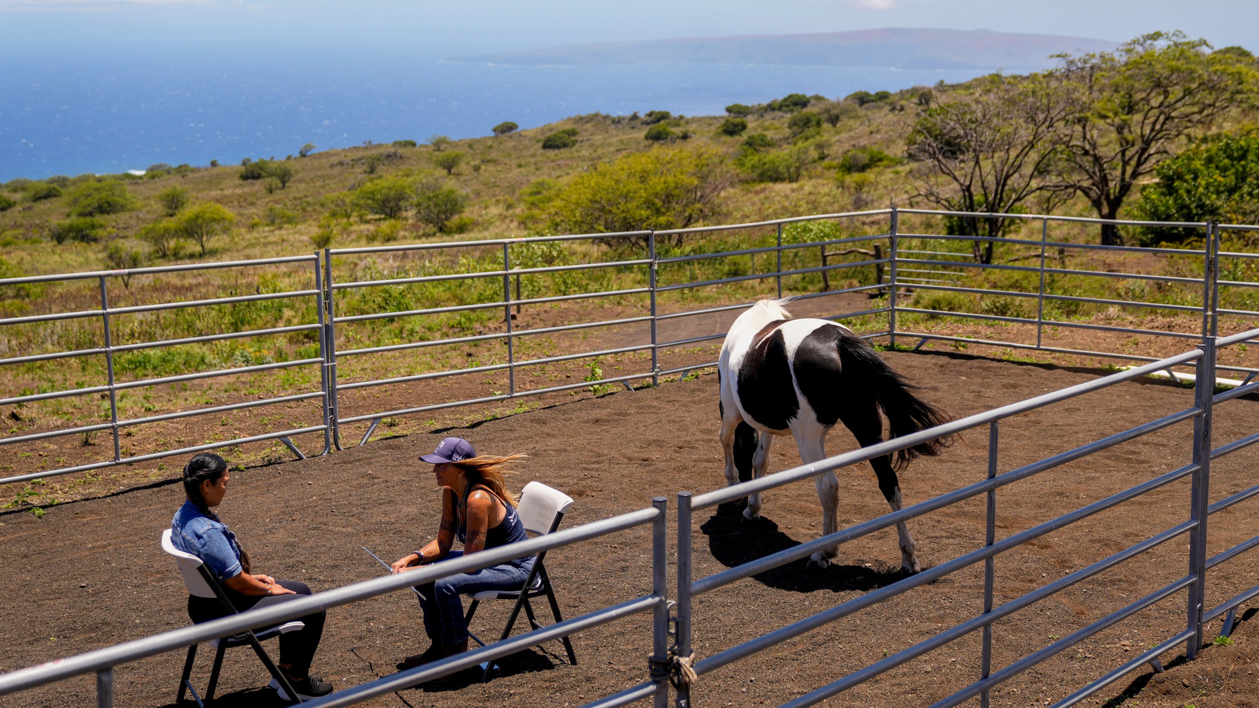 Janice Dapitan, left, speaks with Paige DePonte as a horse named Maverick stands nearby, as part of a philanthropy-supported equine therapy program at the Spirit Horse Ranch, on Tuesday, July 9, 2024, in Kula, Hawaii. (AP Photo/Lindsey Wasson)