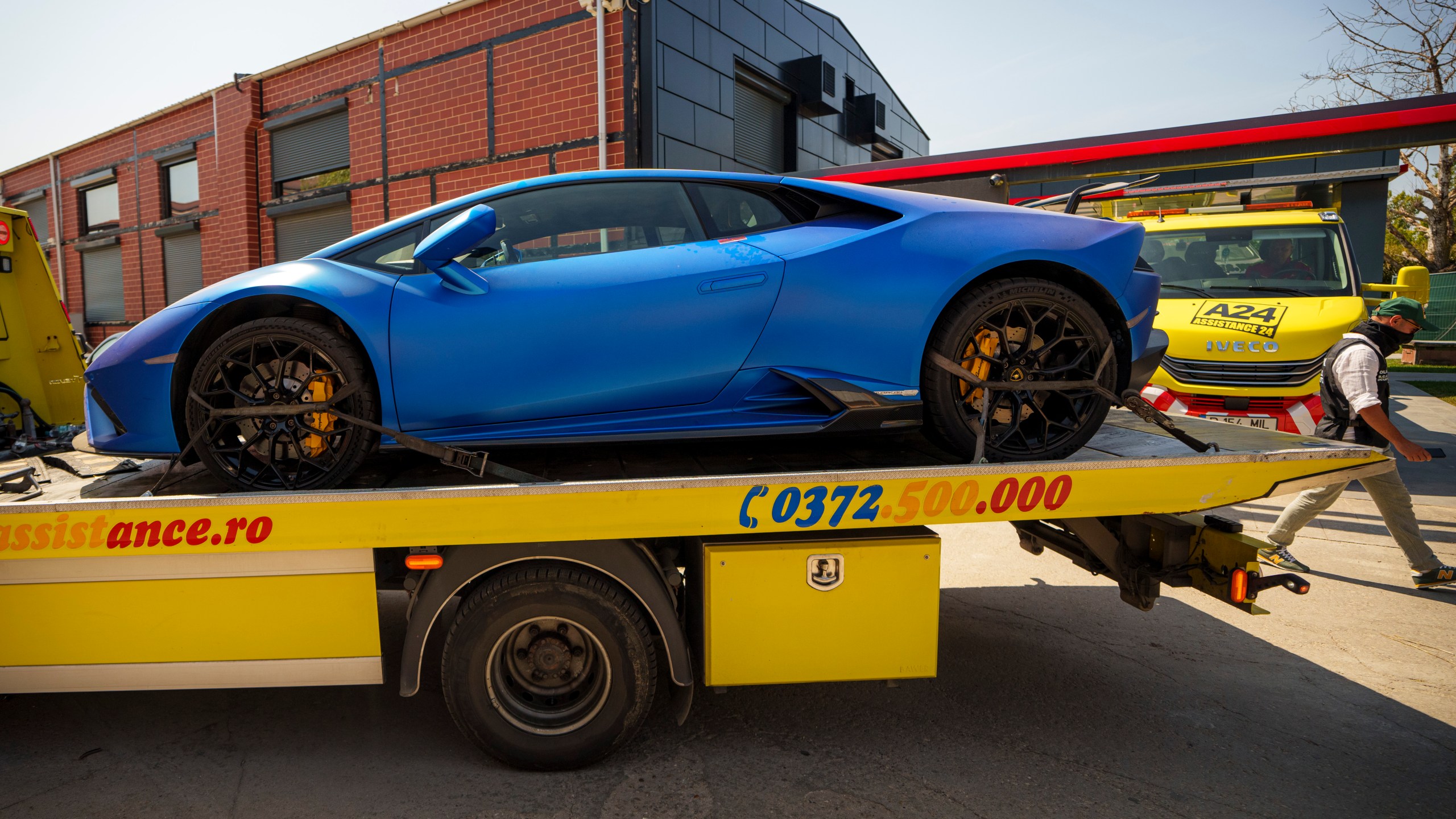 A masked police officer walks as a Lamborghini car is removed by authorities from Andrew Tate's residence on the outskirts of Bucharest, Romania, Saturday, Aug. 24, 2024. (AP Photo/Vadim Ghirda)