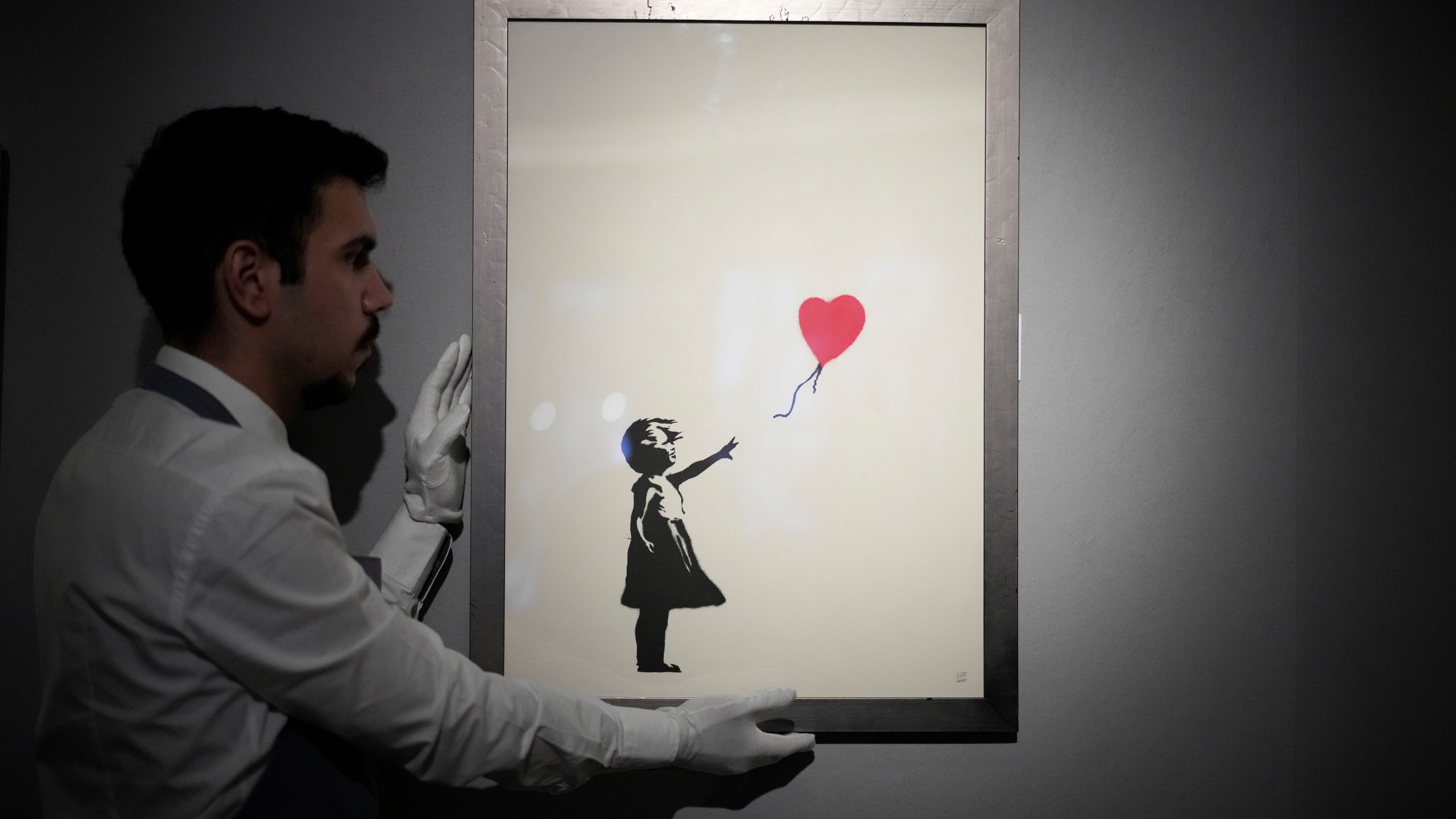 FILE - A staff member poses for photographs with a print of "Girl with Balloon, 2004" by British street artist Banksy, at Bonhams auction house in London, Monday, Nov. 8, 2021. (AP Photo/Matt Dunham, File)