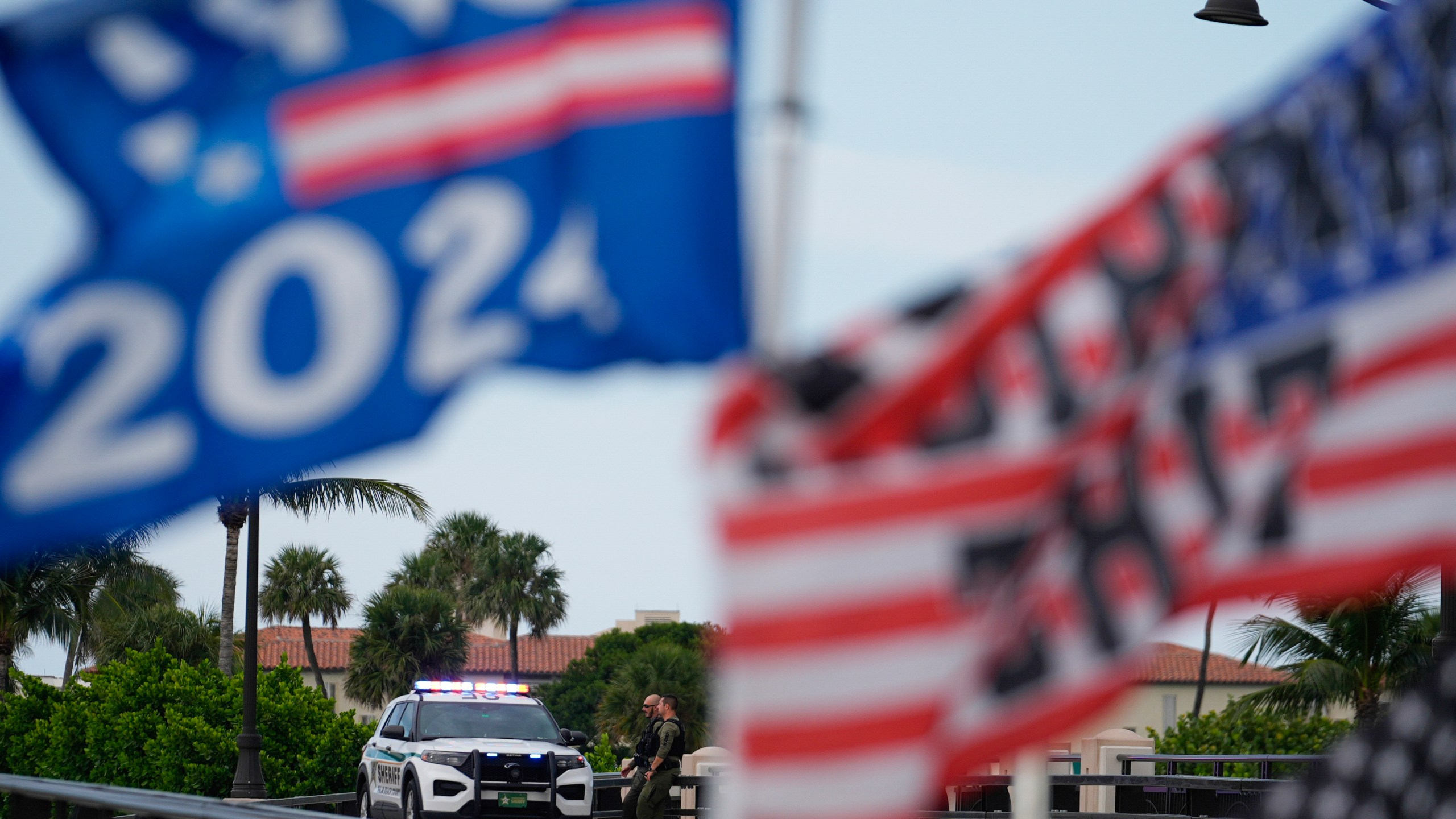 Police patrol on a bridge beside the Mar-a-Lago estate of Republican presidential nominee and former President Donald Trump, as a supporter flies flags to express support for Trump one day after an apparent assassination attempt, in Palm Beach, Fla., Monday, Sept. 16, 2024. (AP Photo/Rebecca Blackwell)