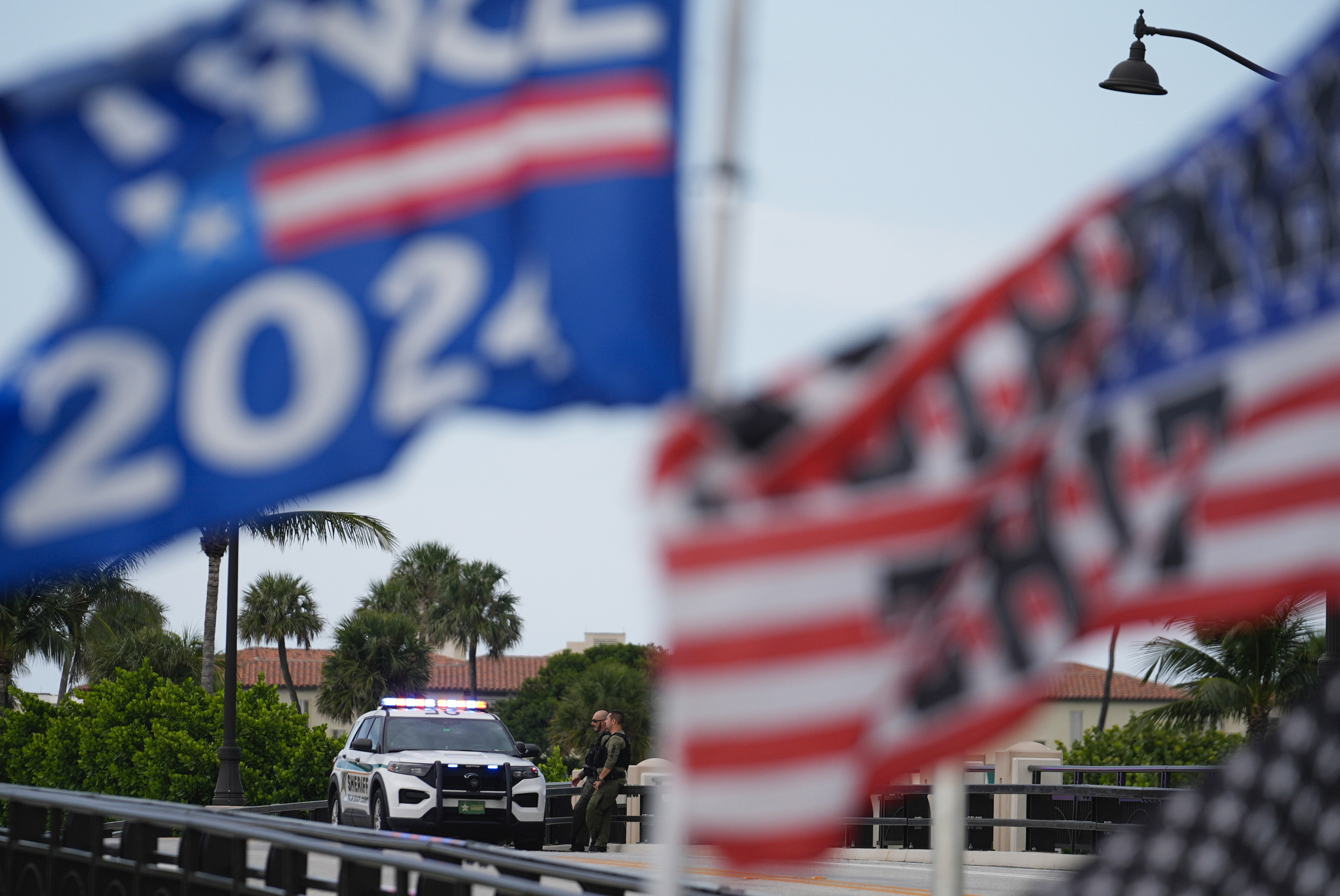 Police patrol on a bridge beside the Mar-a-Lago estate of Republican presidential nominee and former President Donald Trump, as a supporter flies flags to express support for Trump one day after an apparent assassination attempt, in Palm Beach, Fla., Monday, Sept. 16, 2024. (AP Photo/Rebecca Blackwell)