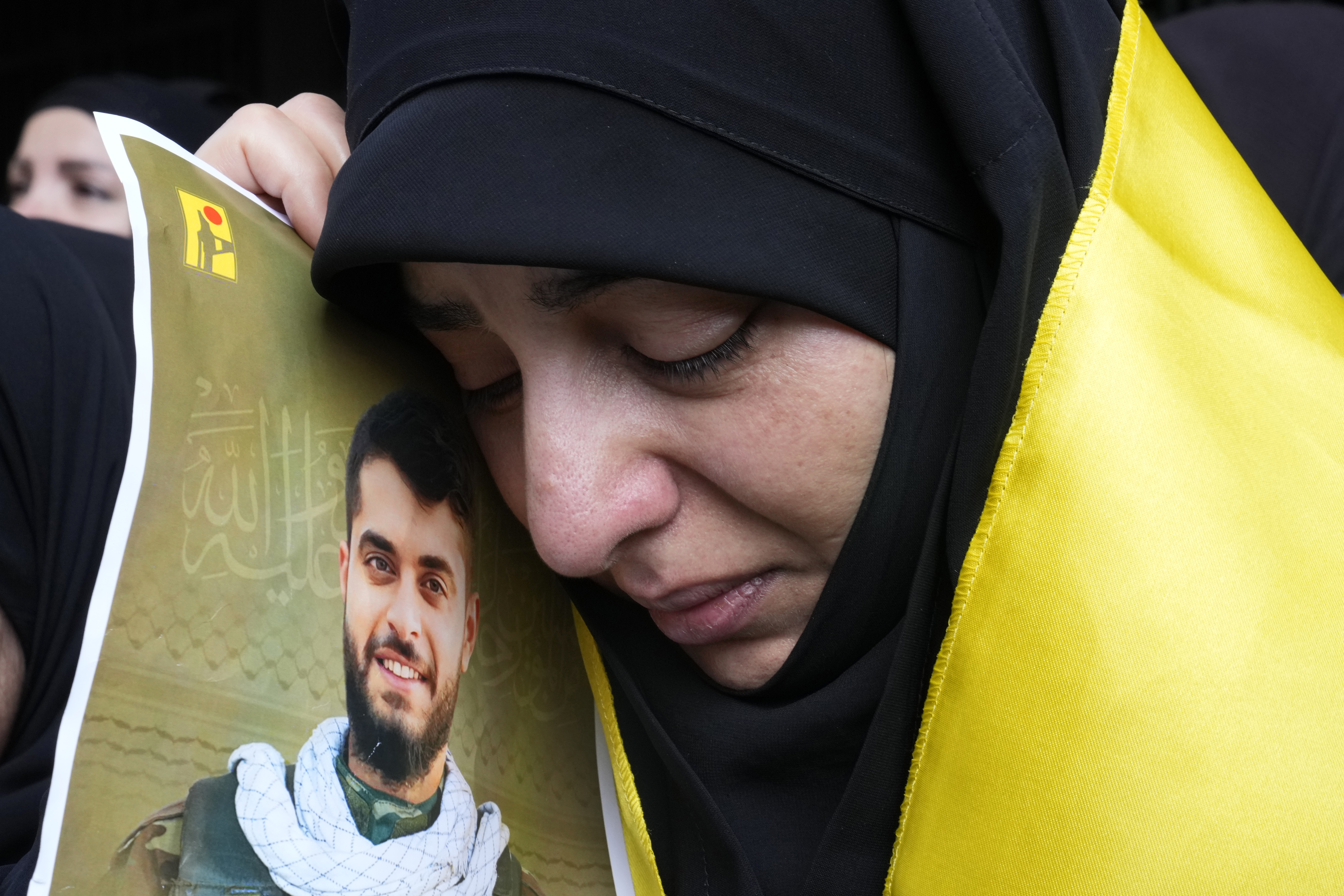 A woman holds a picture of a Hezbollah member who was killed on Wednesday when a handheld device exploded, during his funeral procession in the southern suburbs of Beirut, Thursday, Sept. 19, 2024. (AP Photo/Hussein Malla)