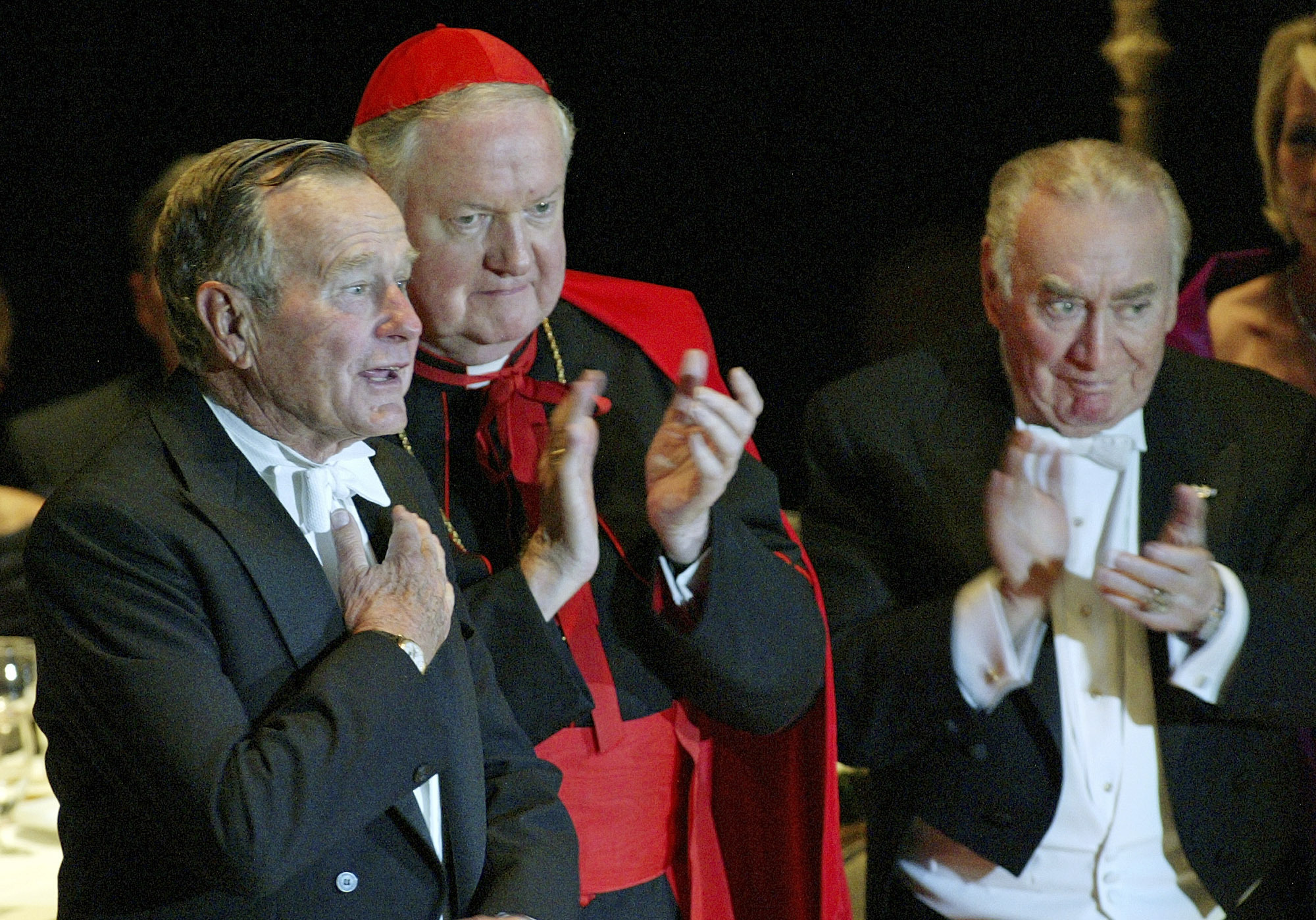 FILE - Former President George H.W. Bush, left, is applauded by Archbishop of New York Cardinal Edward Egan and former Governor of the State of New York Hugh L. Carey, right, after Bush spoke at the 59th annual Alfred E. Smith Memorial Foundation Dinner at the Waldorf Astoria hotel in New York, Thursday, Oct 21, 2004. (AP Photo/Stuart Ramson, File)