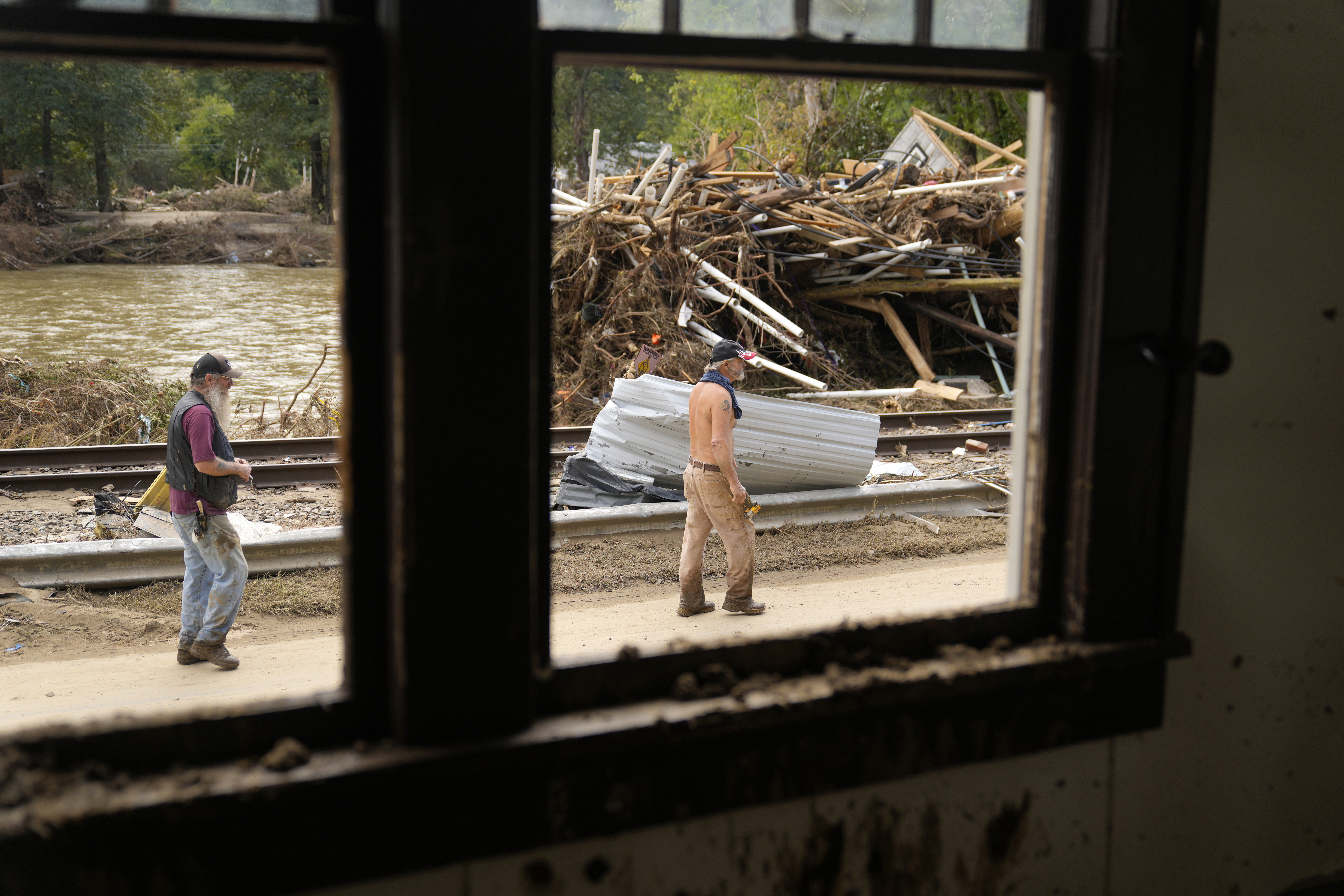 FILE - People walk by a pile of debris left in the wake of Hurricane Helene, Oct. 1, 2024, in Marshall, N.C. (AP Photo/Jeff Roberson, File)