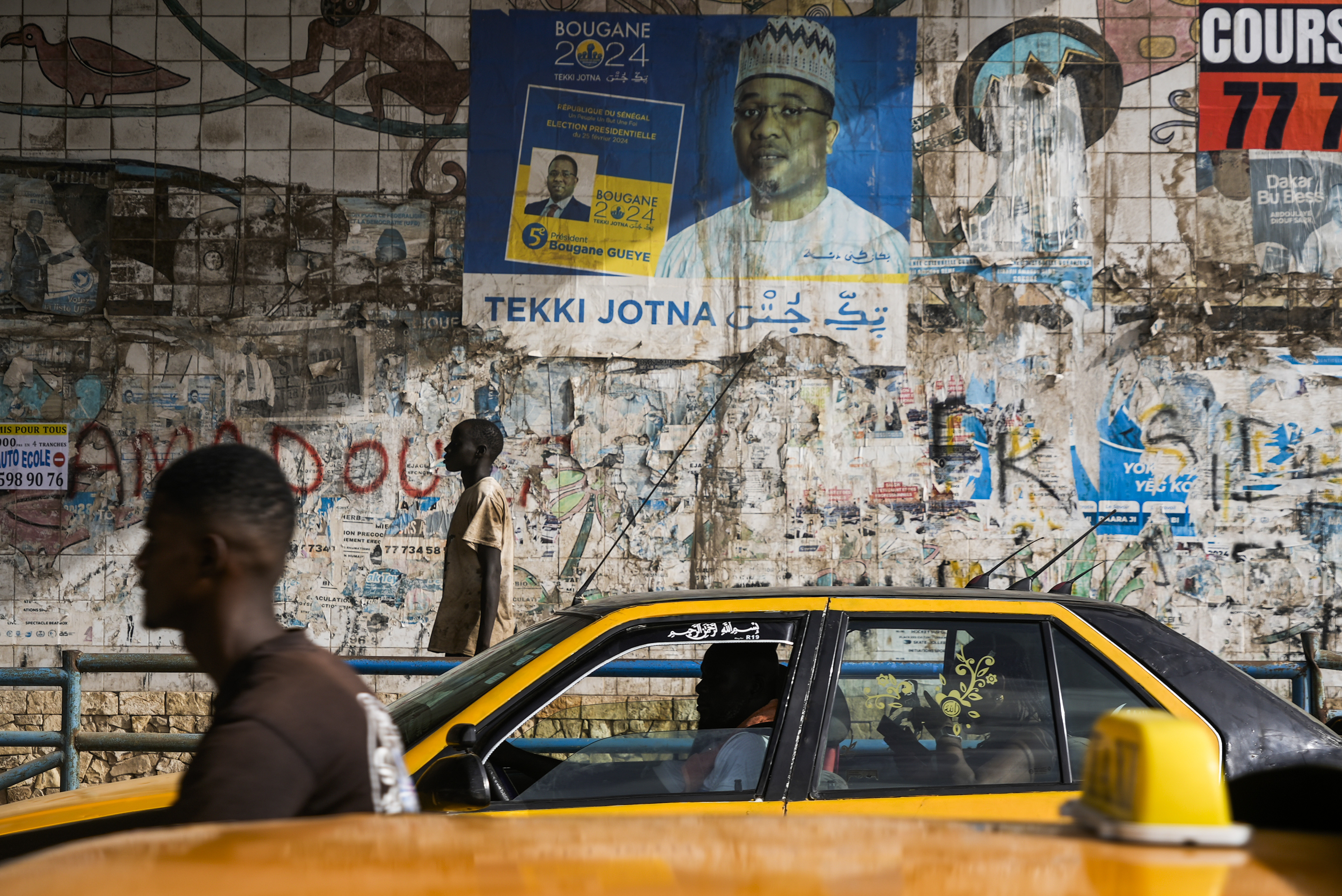 A man walks in front of posters written in Wolof in Dakar, Senegal, Wednesday, Oct. 2, 2024. (AP Photo/Annie Risemberg)