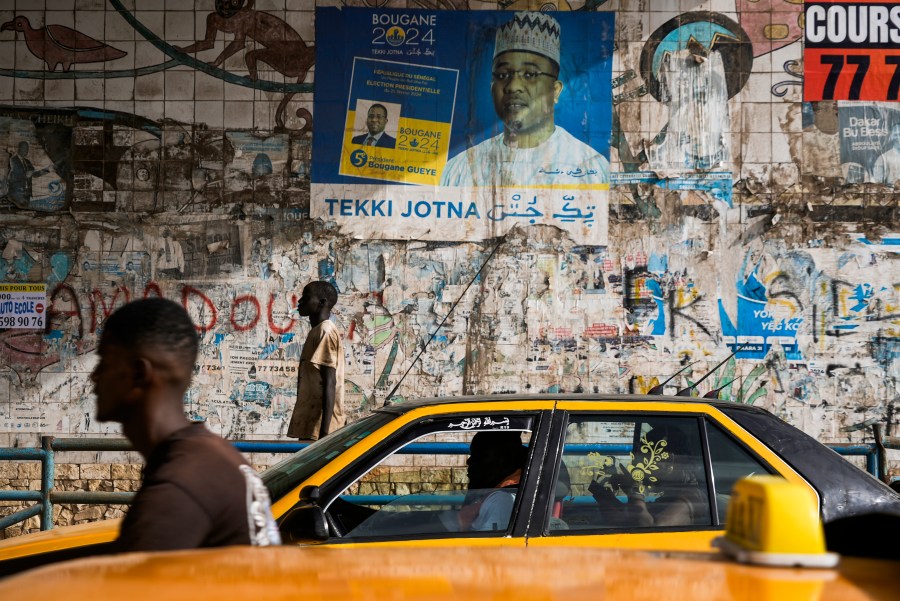 A man walks in front of posters written in Wolof in Dakar, Senegal, Wednesday, Oct. 2, 2024. (AP Photo/Annie Risemberg)