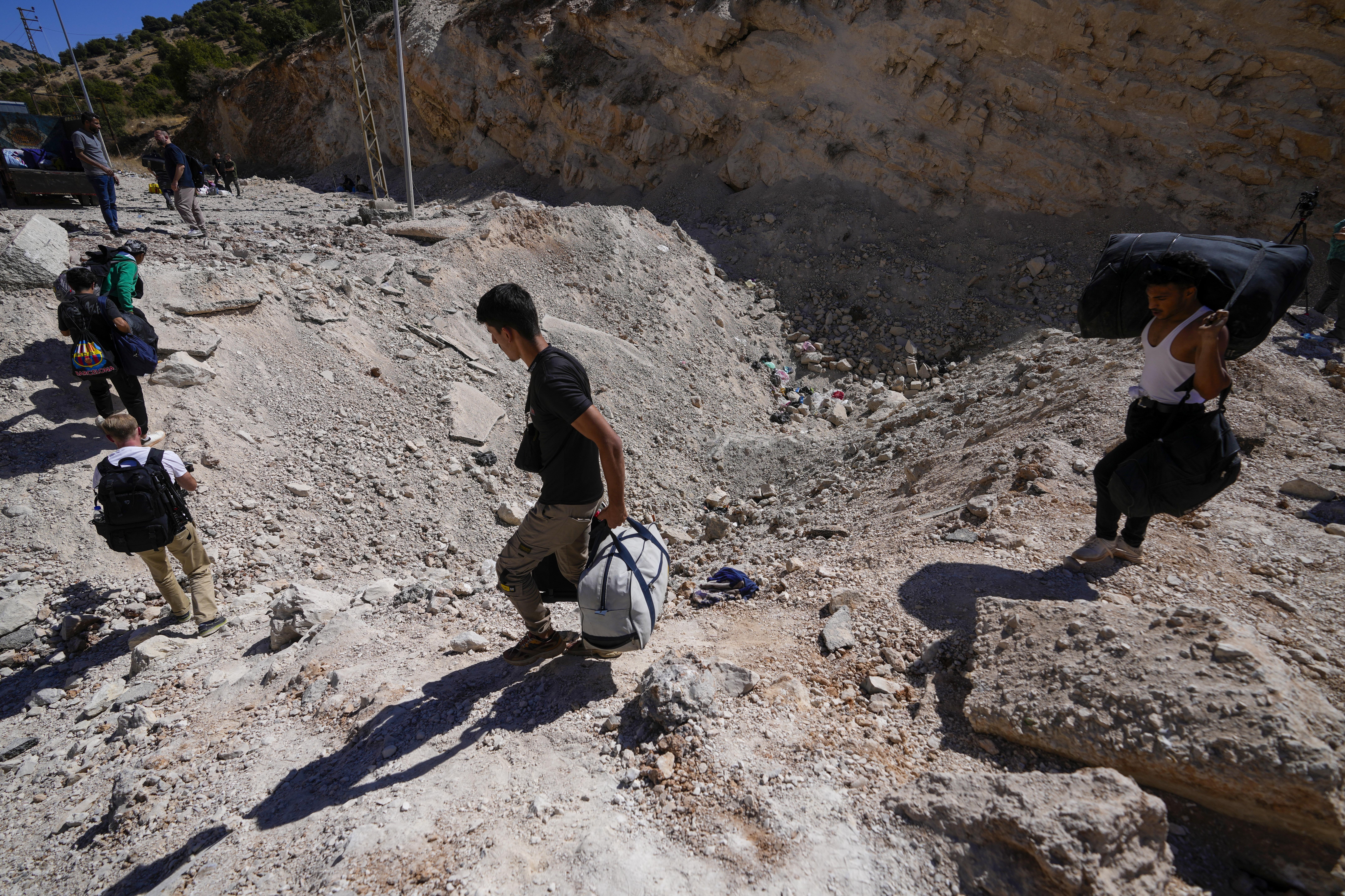 People carry their luggage as they cross into Syria on foot, through a crater caused by Israeli airstrikes aiming to block Beirut-Damascus highway at the Masnaa crossing, in the eastern Bekaa Valley, Lebanon, Saturday, Oct. 5, 2024. (AP Photo/Hassan Ammar)