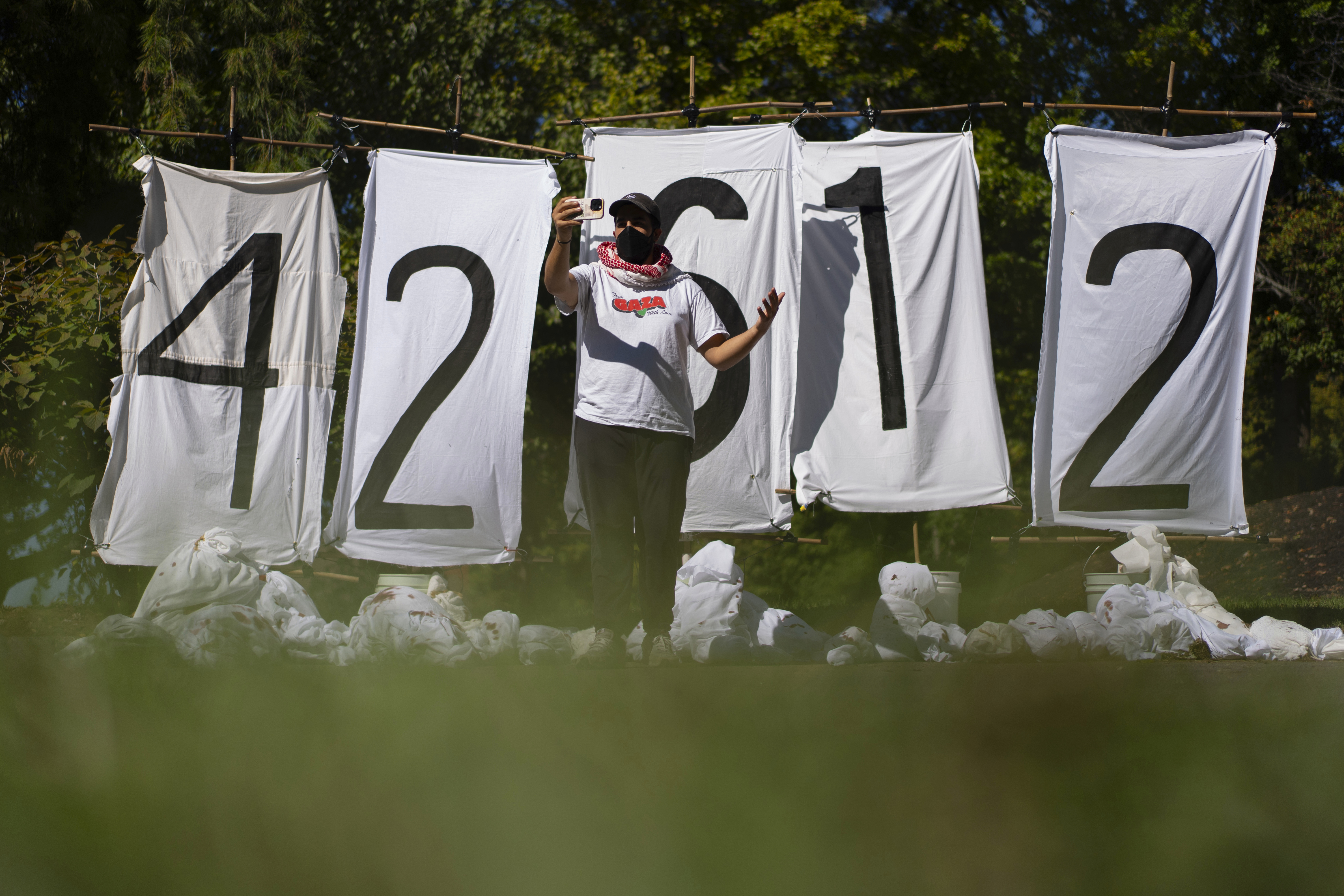 Mike Madanat speaks during a cell phone interview in front of a display of the number of people who have died in Gaza, near the driveway of Ohio Democratic Rep. Greg Landsman's Cincinnati residence, Monday, Oct. 7, 2024. (AP Photo/Carolyn Kaster)