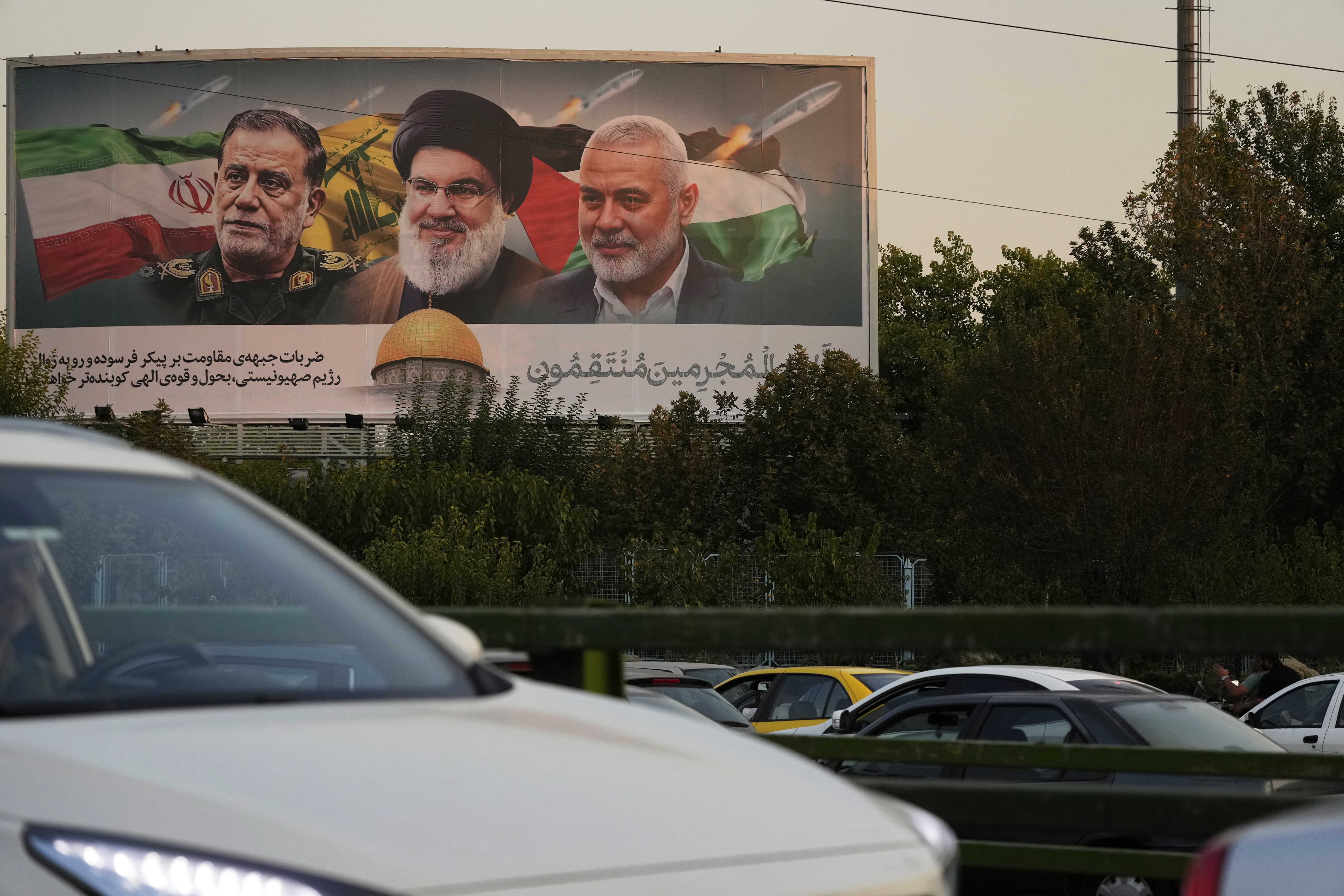 Vehicles drive past a billboard on a highway in Tehran, Iran, Monday, Oct. 7, 2024, showing slain Hezbollah leader Hassan Nasrallah, center, late Hamas leader Ismail Haniyeh, right, and the late Iranian Revolutionary Guard Gen. Abbas Nilforushan, who was killed in an Israeli airstrike. The billboard contains a verse of Quran that reads: "We will surely inflict punishment upon the wicked." (AP Photo/Vahid Salemi)