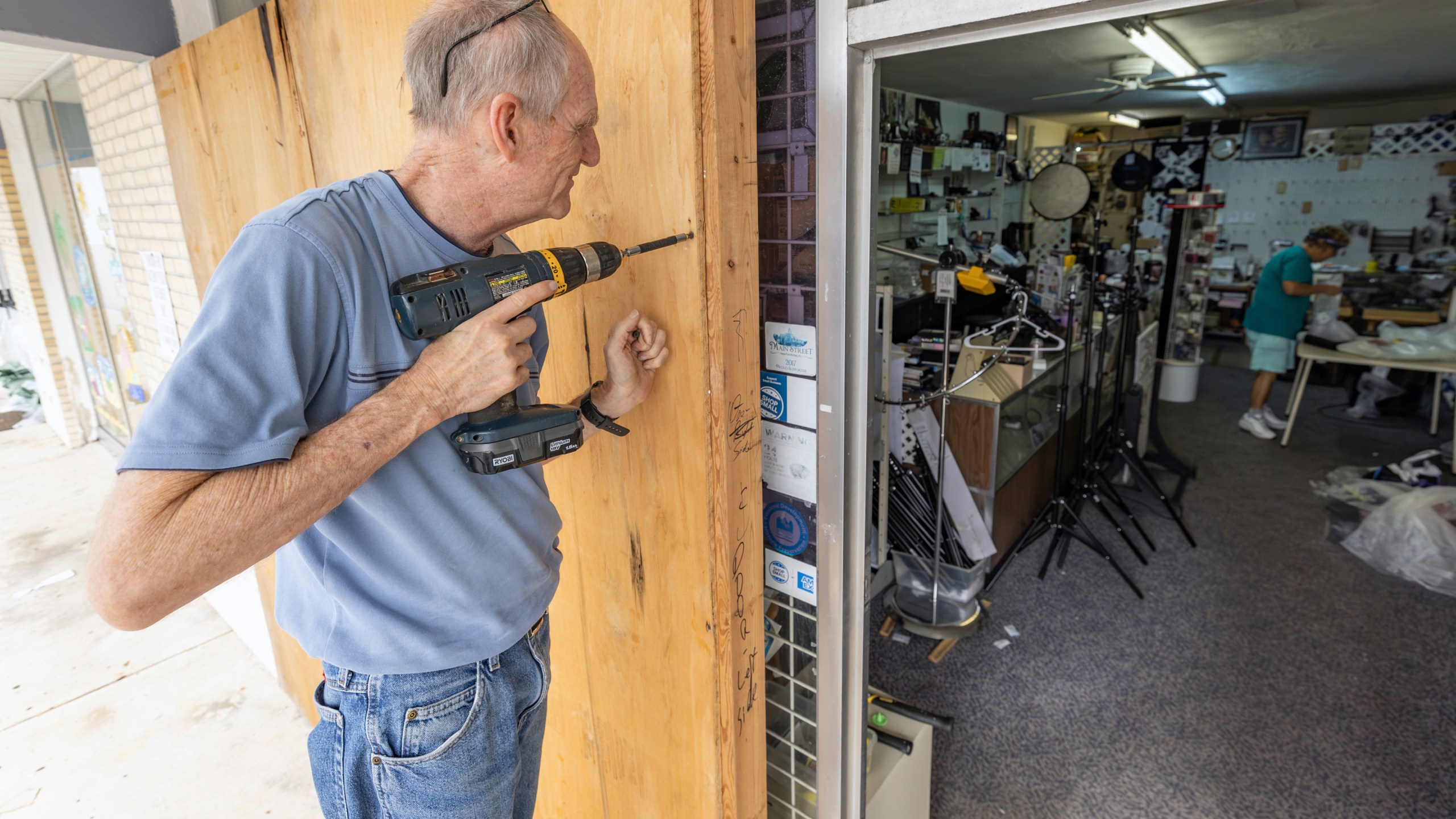 Jim Smetzer puts up boards as his wife Annette clears merchandise from their camera store in preparation for Hurricane Milton on Tuesday, Oct. 8, 2024, in New Port Richey, Fla. (AP Photo/Mike Carlson)