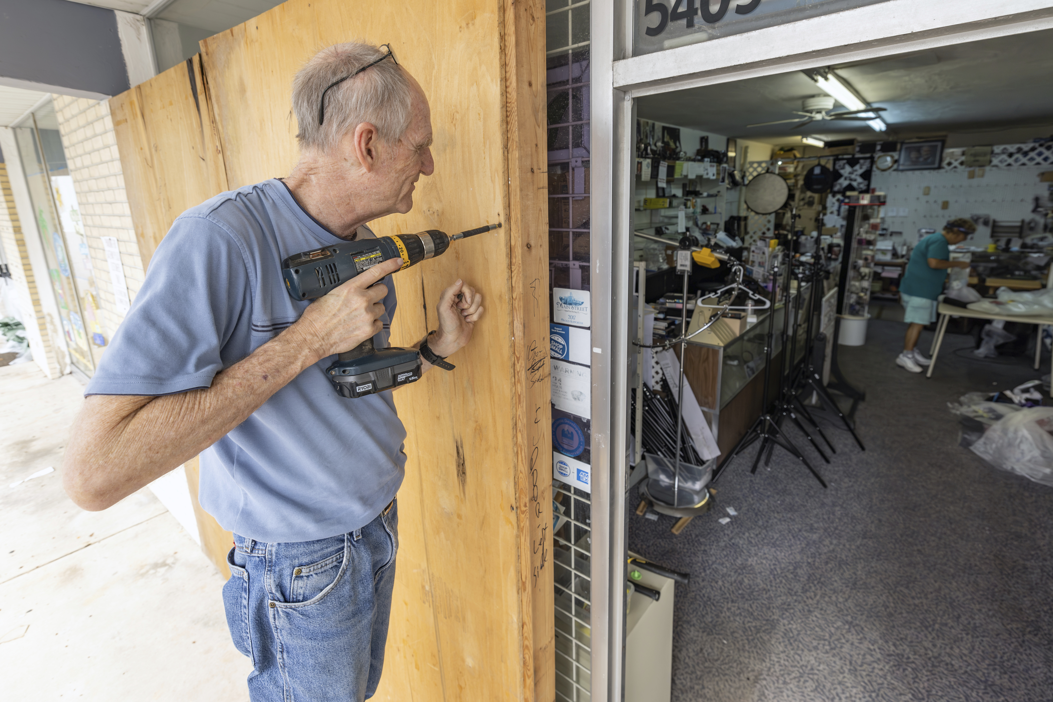 Jim Smetzer puts up boards as his wife Annette clears merchandise from their camera store in preparation for Hurricane Milton on Tuesday, Oct. 8, 2024, in New Port Richey, Fla. (AP Photo/Mike Carlson)