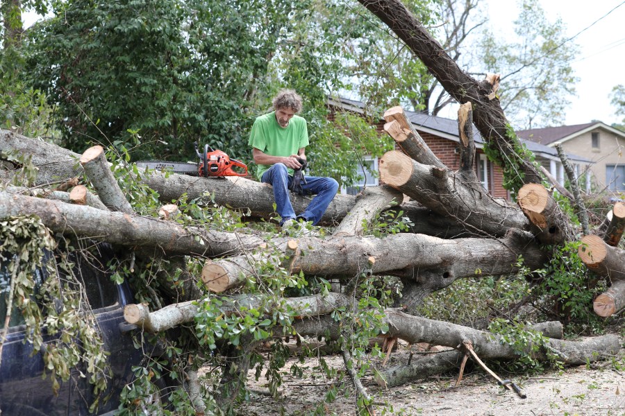 Andy Brown takes a break on top of what remains of a tree that destroyed his SUV when it fell during Hurricane Helene on in Augusta, Ga., Tuesday, Oct. 1, 2024. (AP Photo/Jeffrey Collins)