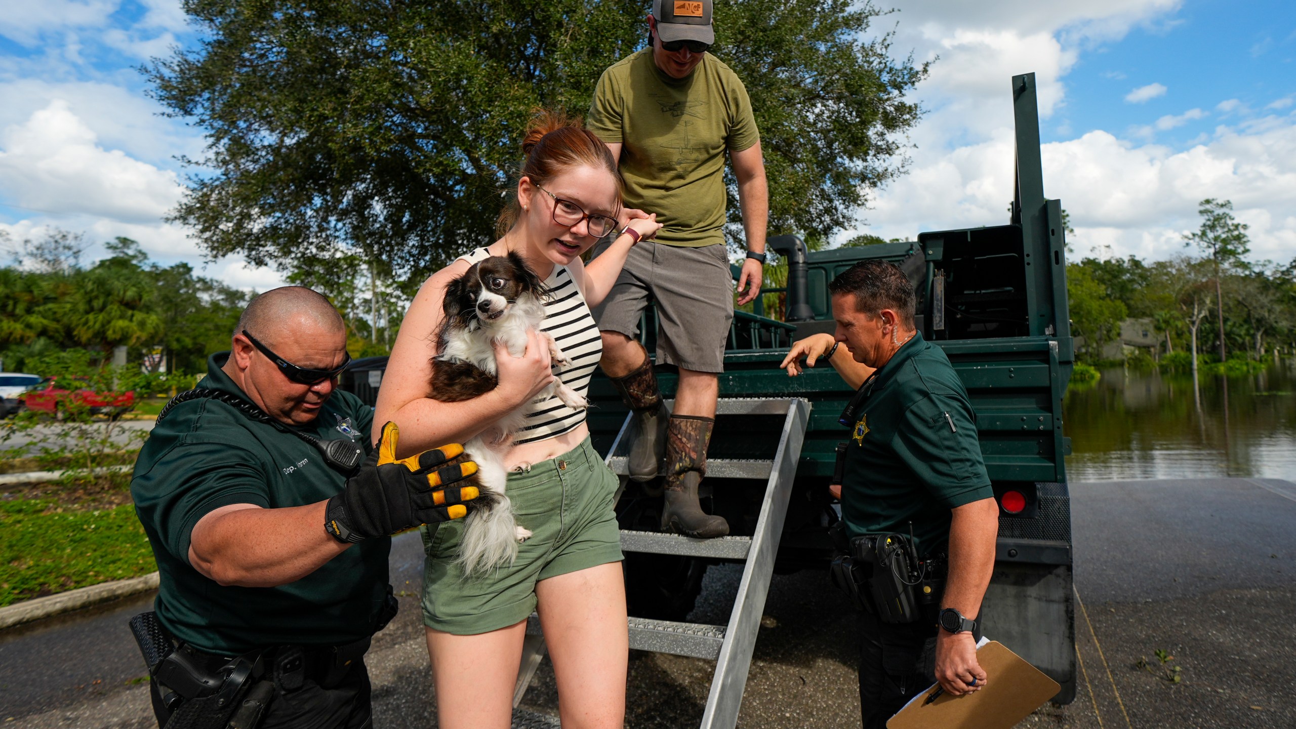 Sarah McRee holds a dog named Poe as she is helped off a high-clearance vehicle by Panellas County Sheriff officials after she was escorted in and out of the Tarpon Woods neighborhood as people return to their homes following Hurricane Milton, Friday, Oct. 11, 2024, in Palm Harbor, Fla. (AP Photo/Julio Cortez)