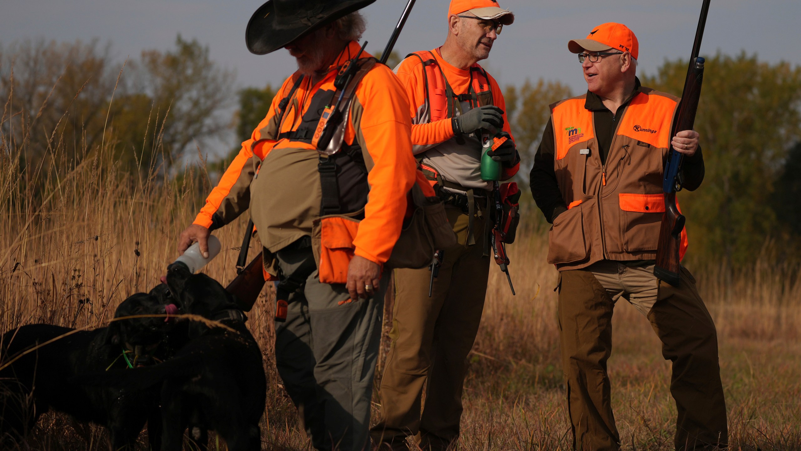 Minnesota Governor and Democratic Vice Presidential candidate Tim Walz talks with Matt Kucharski, as Scott Rall gives water to his three hunting dogs, during the annual Minnesota Governor's Pheasant Hunting Opener, Saturday, Oct. 12, 2024, near Sleepy Eye, Minn. (Anthony Souffle/Star Tribune via AP)