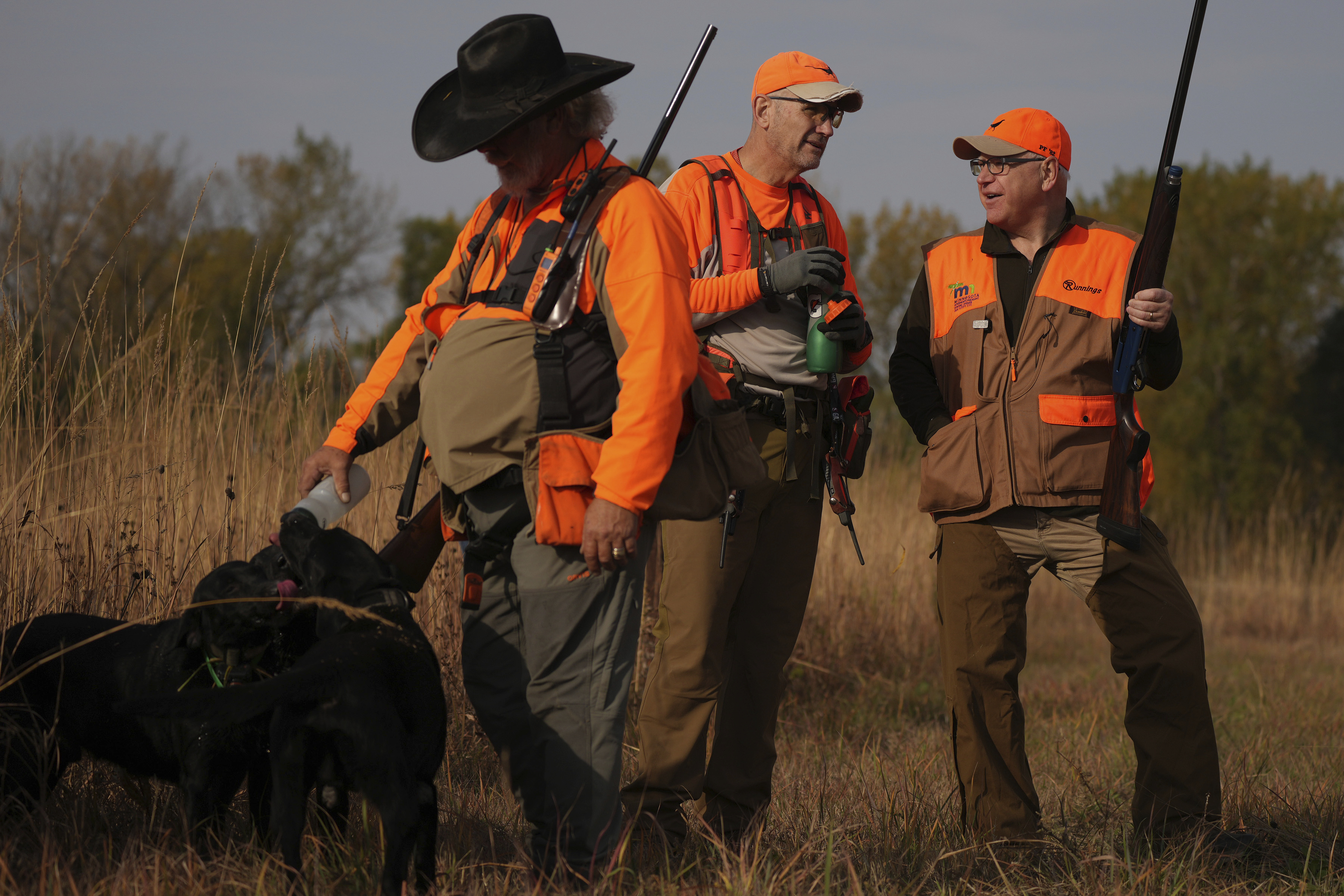 Minnesota Governor and Democratic Vice Presidential candidate Tim Walz talks with Matt Kucharski, as Scott Rall gives water to his three hunting dogs, during the annual Minnesota Governor's Pheasant Hunting Opener, Saturday, Oct. 12, 2024, near Sleepy Eye, Minn. (Anthony Souffle/Star Tribune via AP)