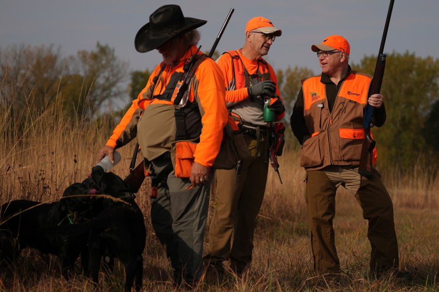 Minnesota Governor and Democratic Vice Presidential candidate Tim Walz talks with Matt Kucharski, as Scott Rall gives water to his three hunting dogs, during the annual Minnesota Governor's Pheasant Hunting Opener, Saturday, Oct. 12, 2024, near Sleepy Eye, Minn. (Anthony Souffle/Star Tribune via AP)