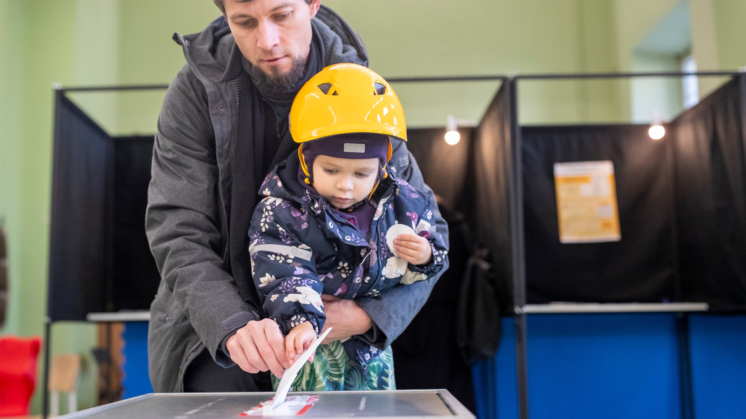 A man with a child casts his ballot at a polling station during the first round of voting in parliamentary elections, in Vilnius, Lithuania, Sunday, Oct. 13, 2024. (AP Photo/Mindaugas Kulbis)