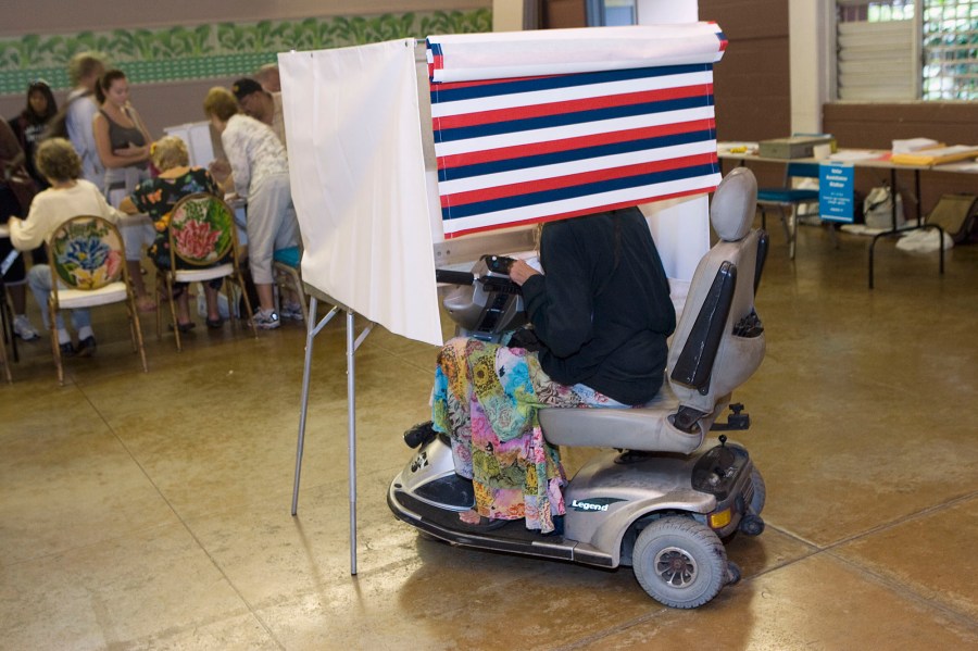 FILE - A woman in a motorized wheelchair casts her vote at the Waikiki Community Center in Honolulu, on Tuesday, Nov. 4 2008. (AP Photo/Marco Garcia, File)