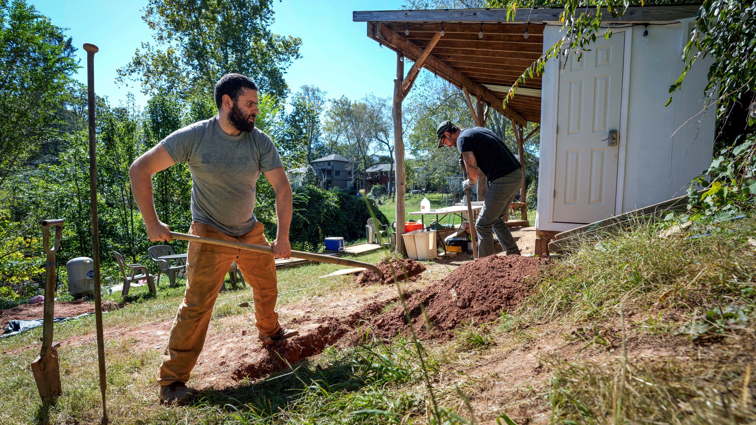 Volunteers, Ben Gordon, left, and Anthony Rubino work on digging a ditch for pipes to offer both nonpotable and potable water for the community, Monday, Oct. 14, 2024, in Asheville, N.C. (AP Photo/Kathy Kmonicek)