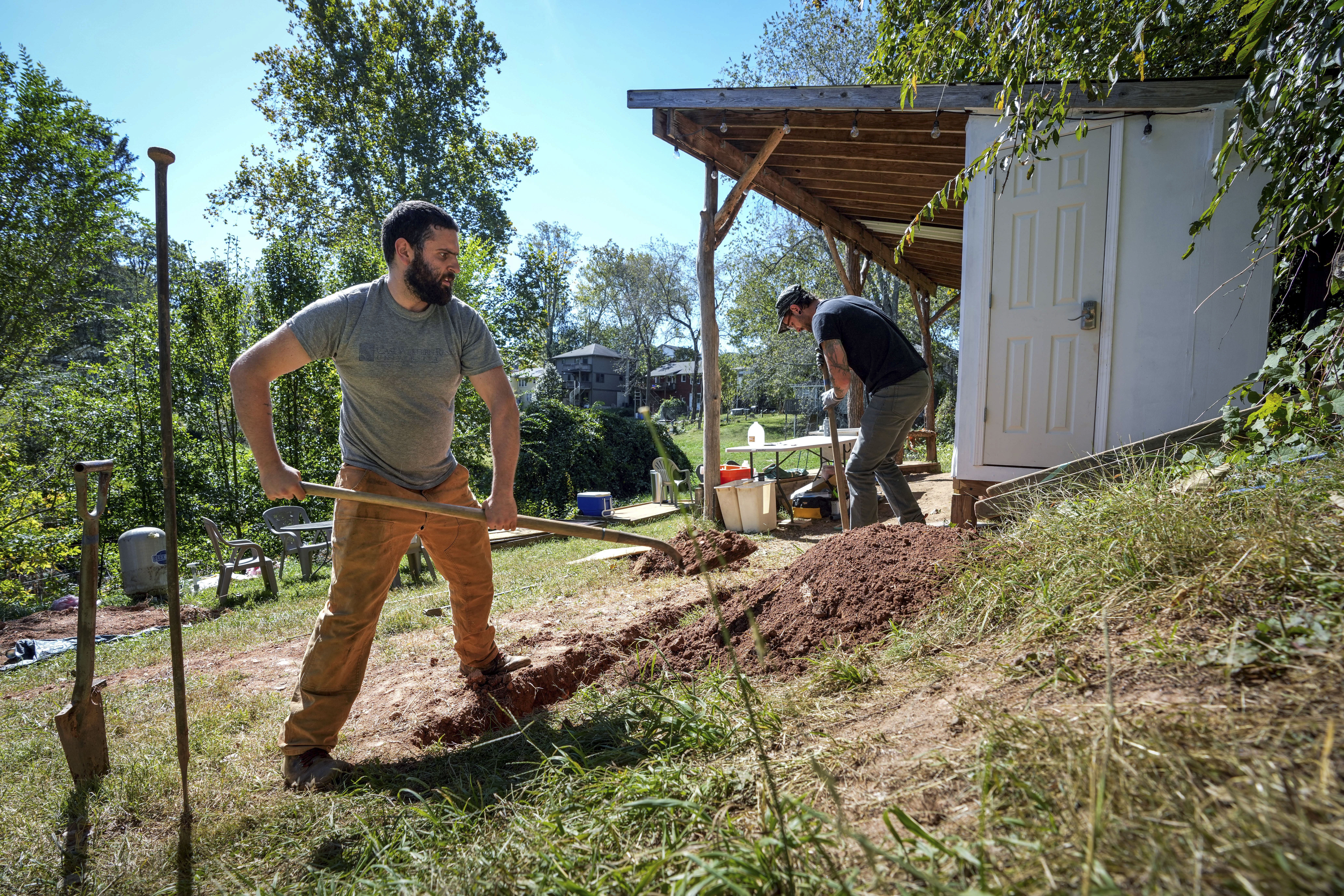 Volunteers, Ben Gordon, left, and Anthony Rubino work on digging a ditch for pipes to offer both nonpotable and potable water for the community, Monday, Oct. 14, 2024, in Asheville, N.C. (AP Photo/Kathy Kmonicek)