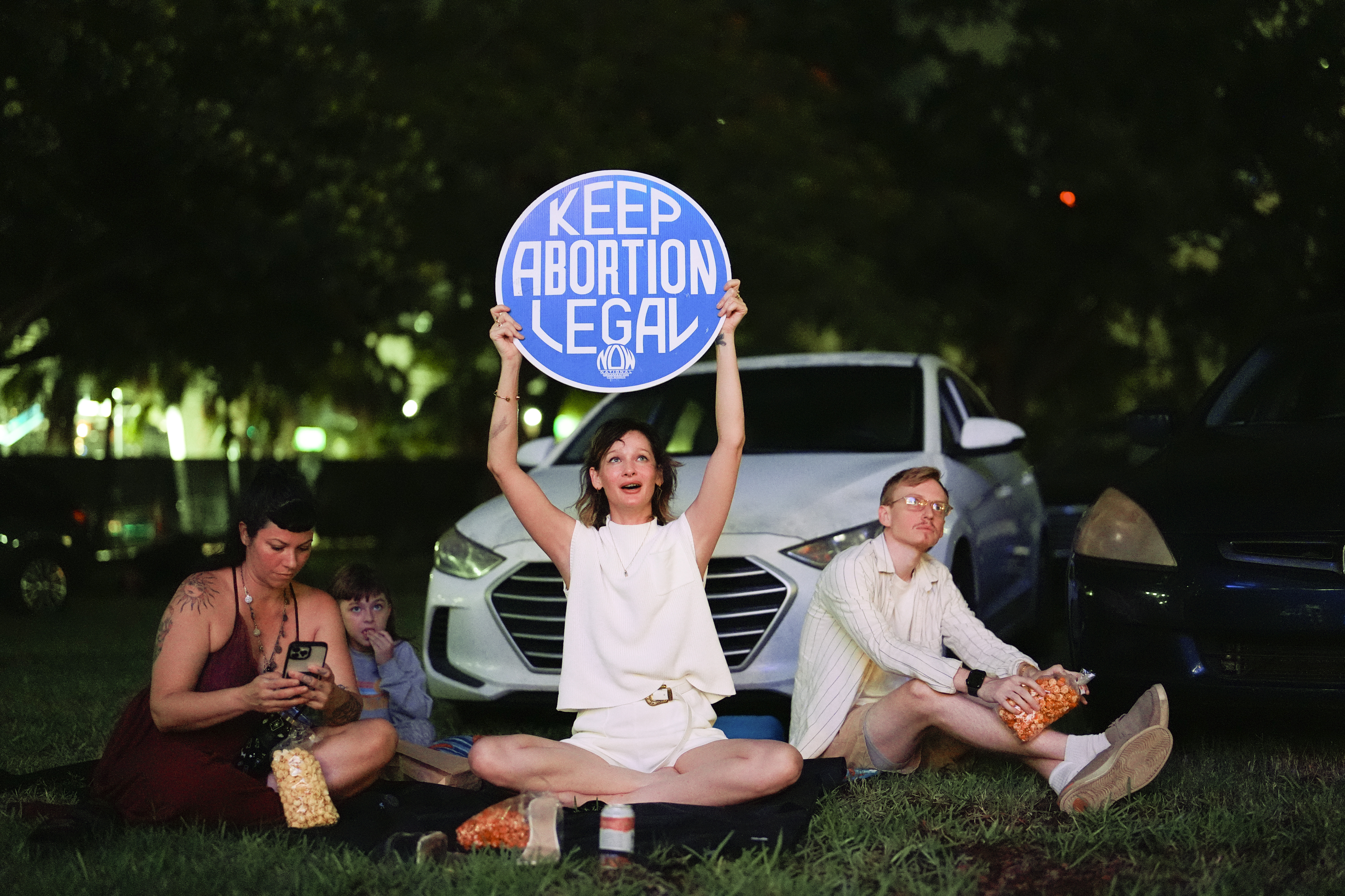 FILE - Reproductive rights advocate Kat Duesterhaus holds up a sign as U.S. President Joe Biden and his Republican rival, former President Donald Trump speak about abortion access, as the the first general election debate of the 2024 season is projected on a outdoor screen at the Nite Owl drive-in theater, Thursday, June 27, 2024, in Miami. (AP Photo/Rebecca Blackwell, File)