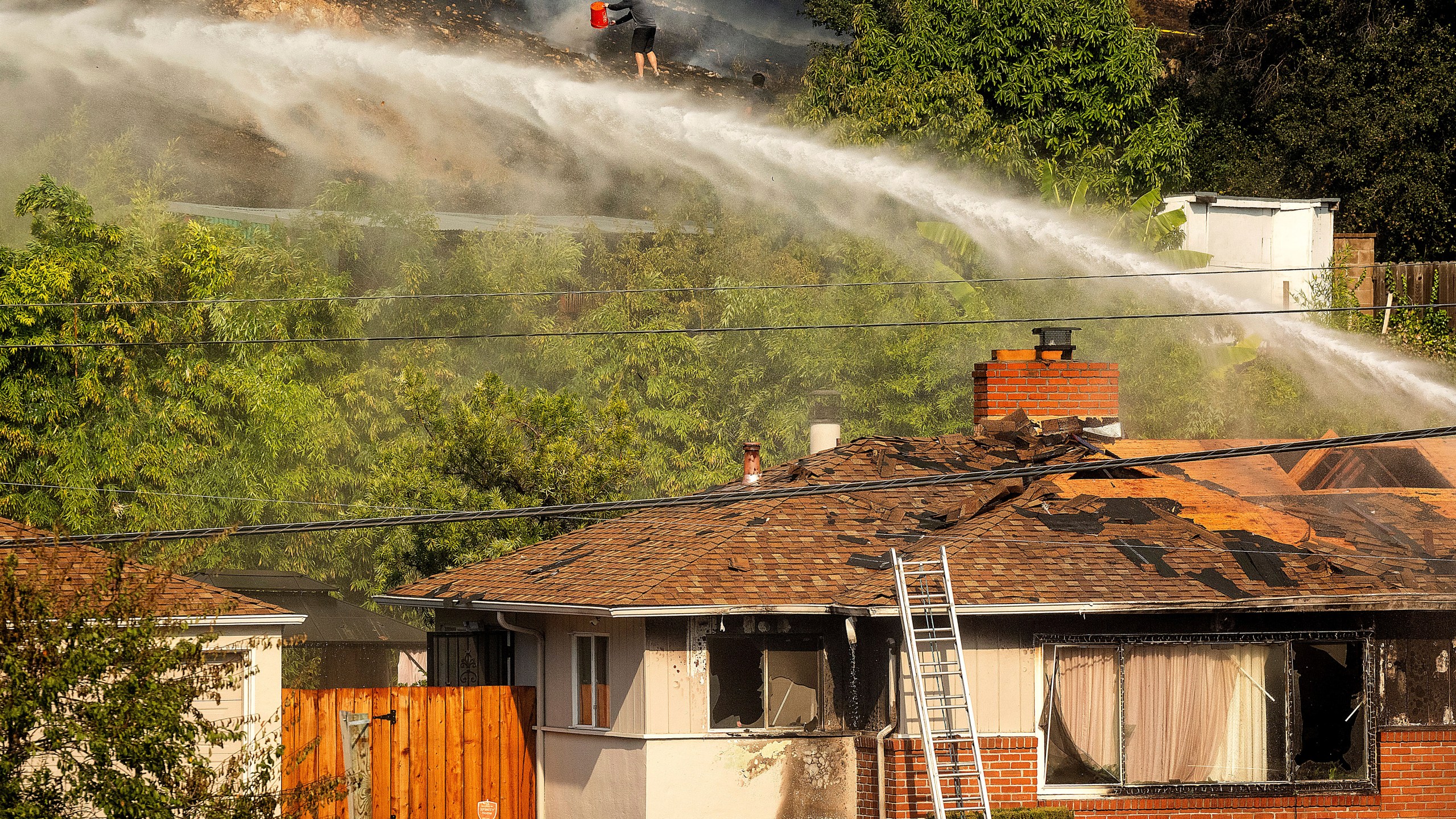 A person dumps water on a grass fire burning above Interstate 580 in Oakland, Calif., Friday, Oct. 18, 2024. (AP Photo/Noah Berger)